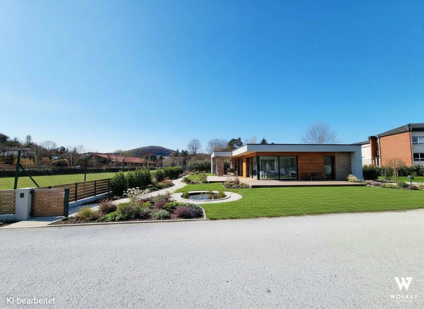 Gepflegter Gartenbereich mit Teich und moderner Hausfassade unter blauem Himmel.