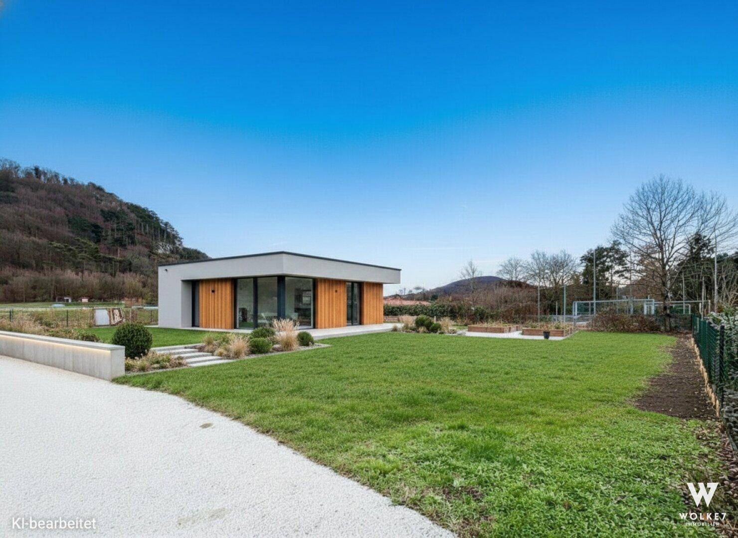 Ansicht des modernen Einfamilienhauses mit weitläufiger Rasenfläche und angrenzendem Hügel.