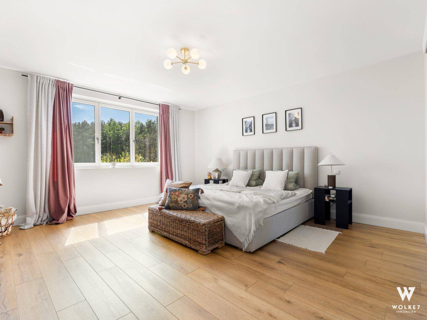 Geräumiges Schlafzimmer mit Holzboden, großem Fenster und Blick ins Grüne.