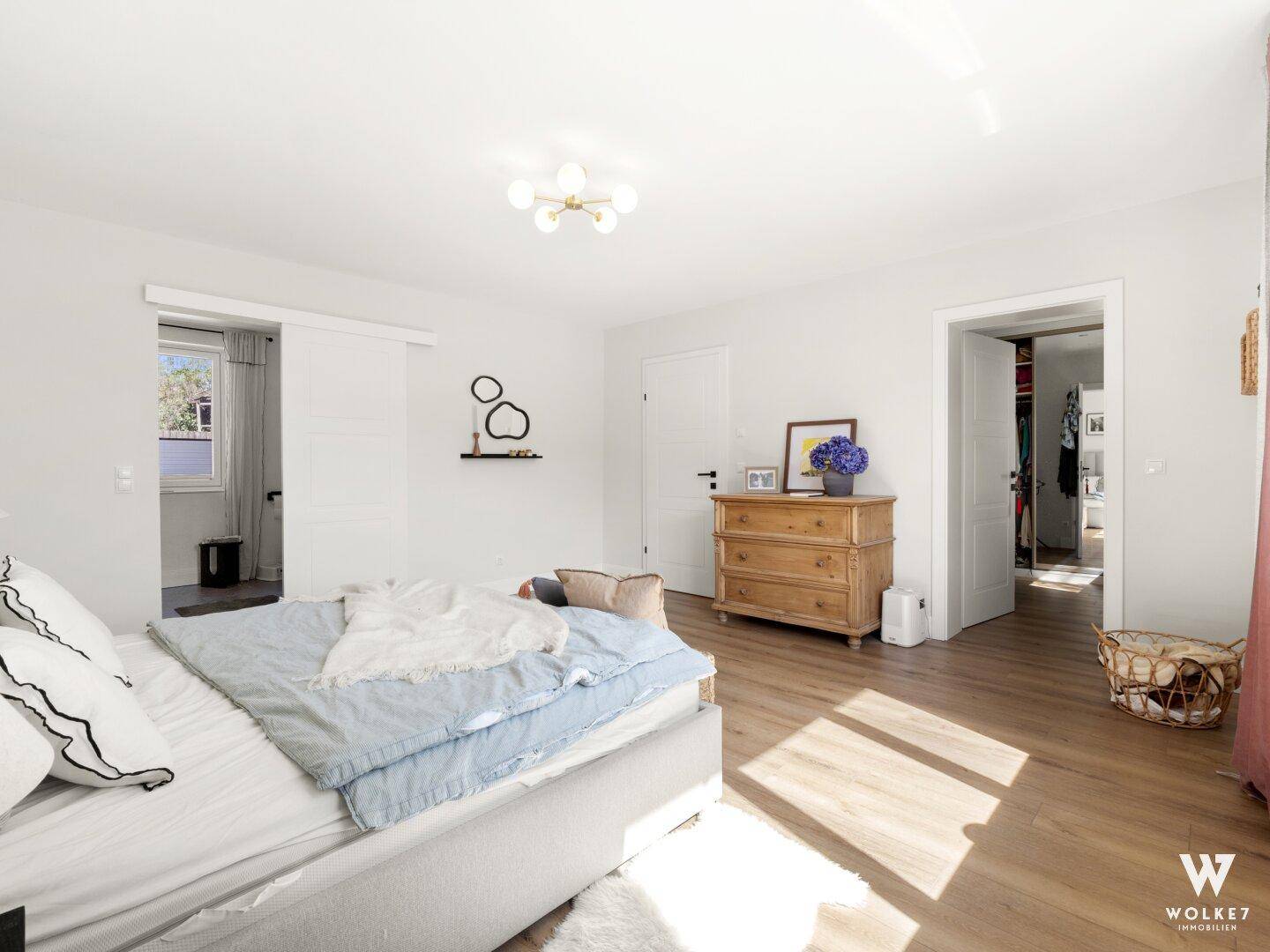 Helles Schlafzimmer mit Holzboden und Schiebetür, die zu einem weiteren Raum führt.