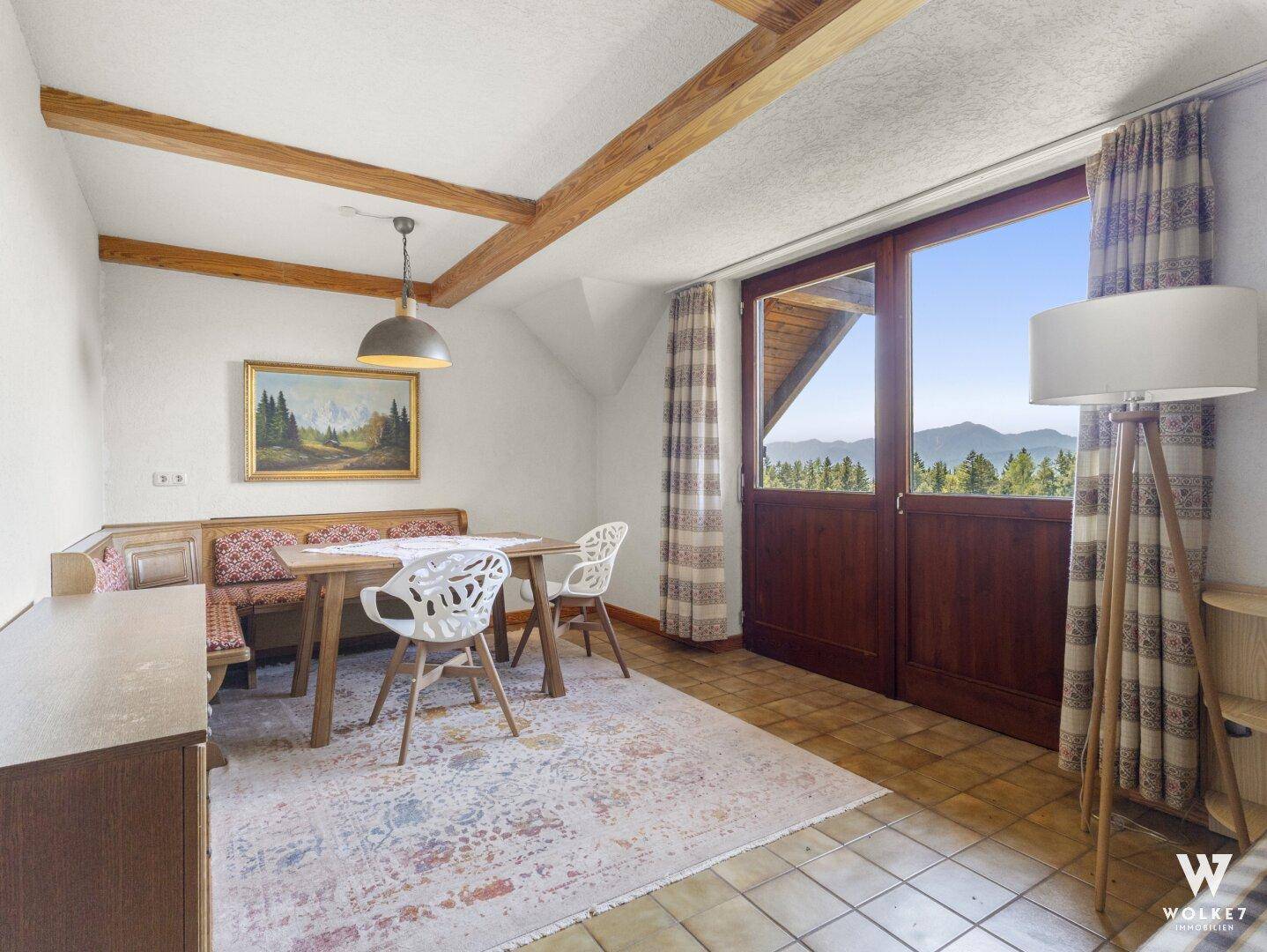 Heller Essbereich mit Holzbalken, gefliestem Boden und Zugang zu einem Balkon mit Bergblick.