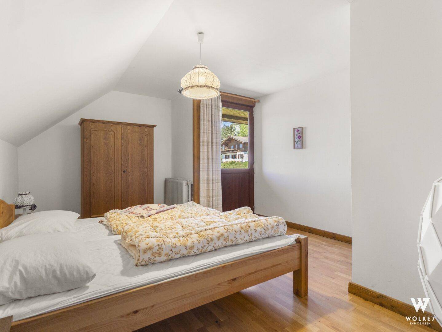 Schlafzimmer mit Holzboden, Dachschräge und Zugang zu einem kleinen Balkon.