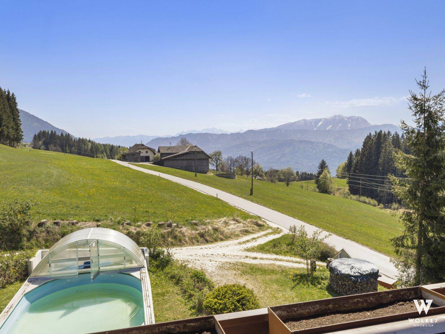 Aussicht vom Balkon auf den Poolbereich und die weite, grüne Landschaft mit Bergen im Hintergrund.