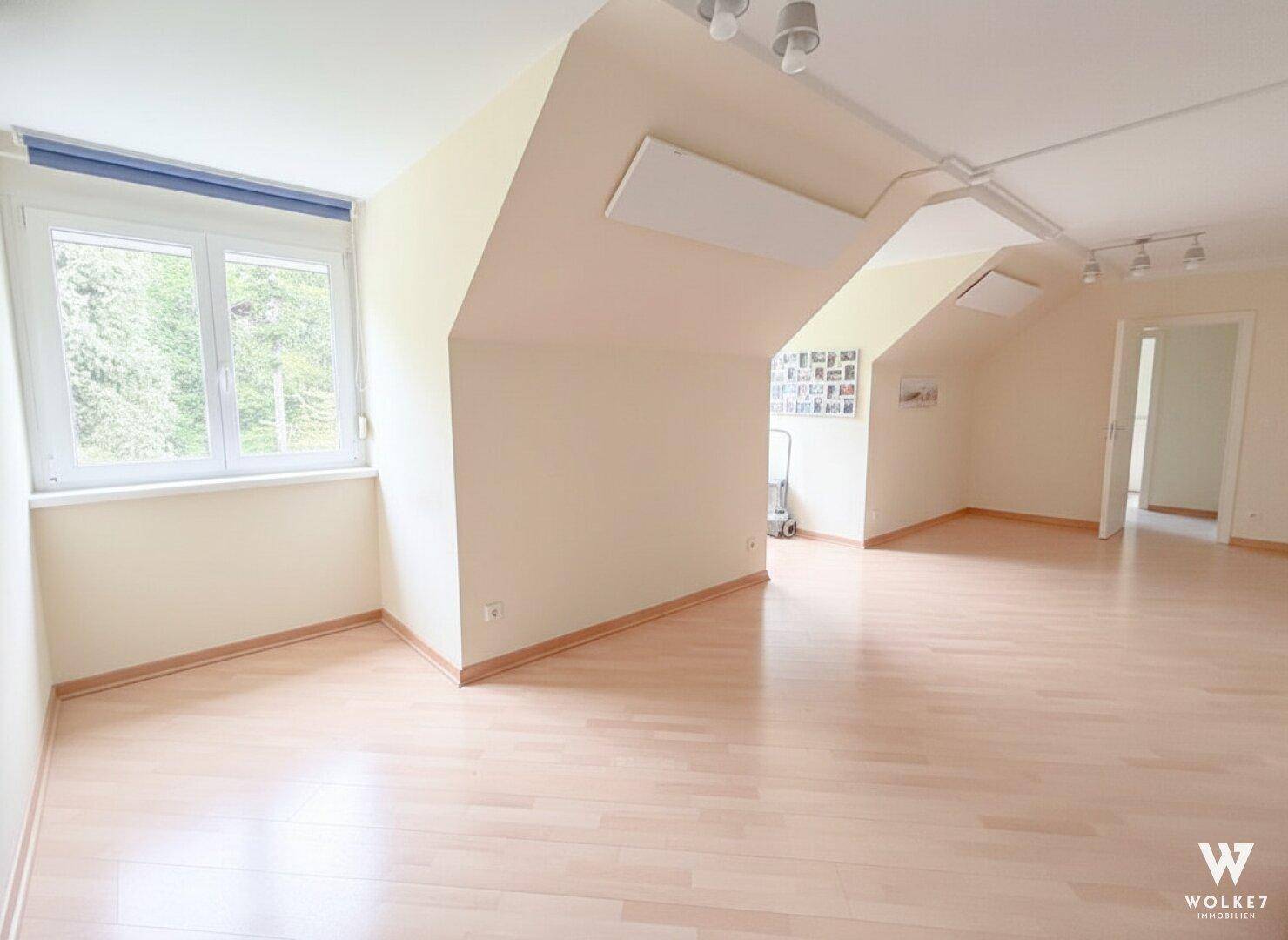 Helles, leeres Wohnzimmer im Dachgeschoss mit großen Fenstern und hellem Holzboden.
