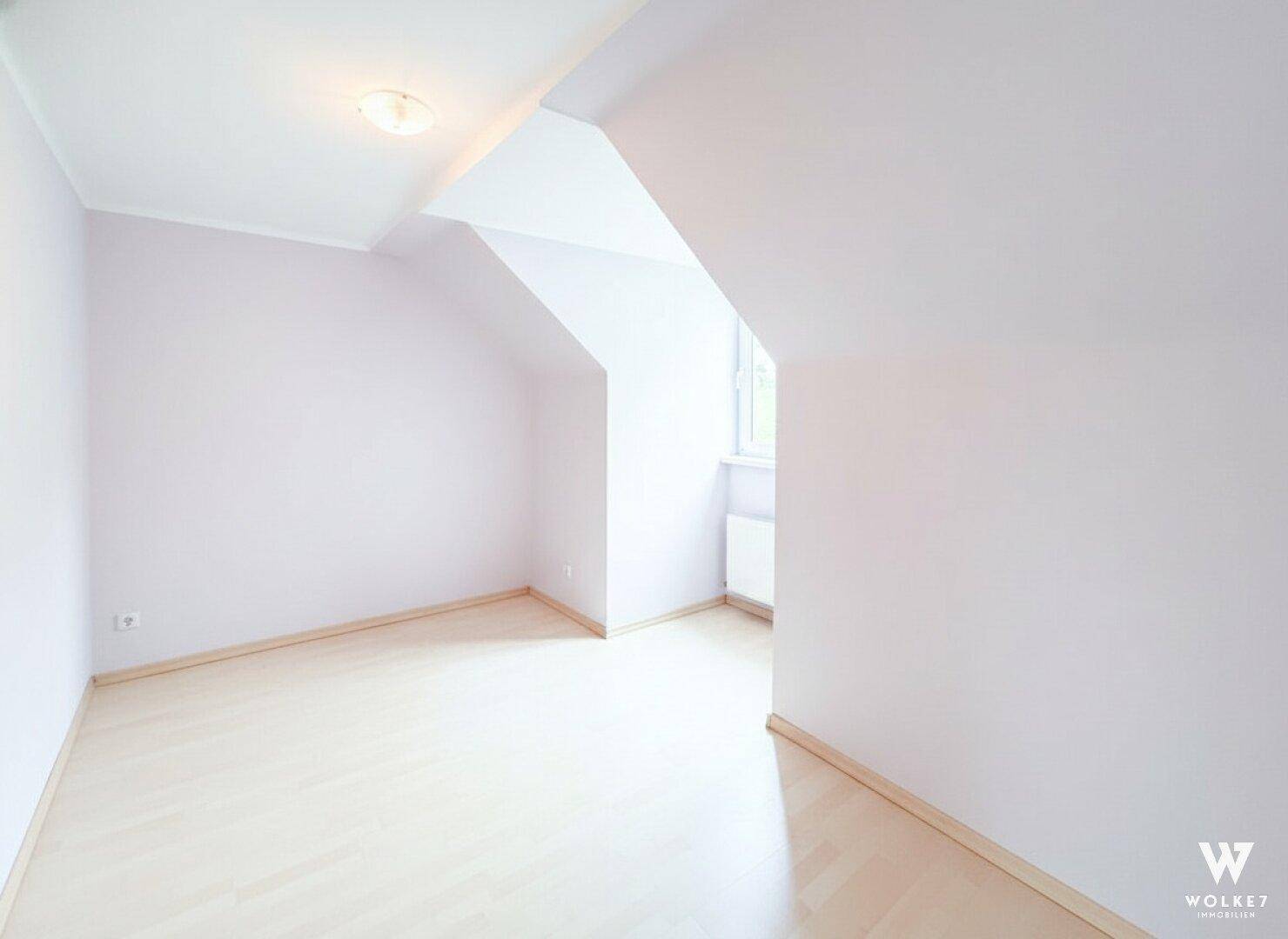 Helles, leeres Schlafzimmer mit Dachschräge und Fenster, ideal für ein Kinderzimmer.