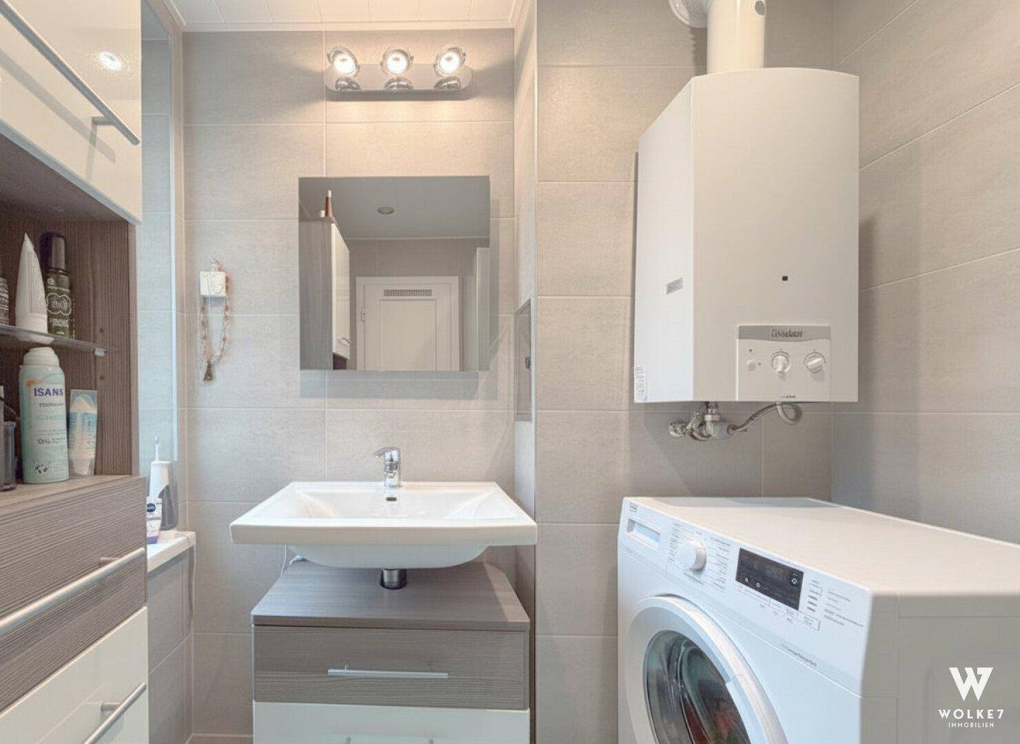 Kleiner Waschraum mit Waschmaschine, Waschbecken und Gastherme an der Wand.