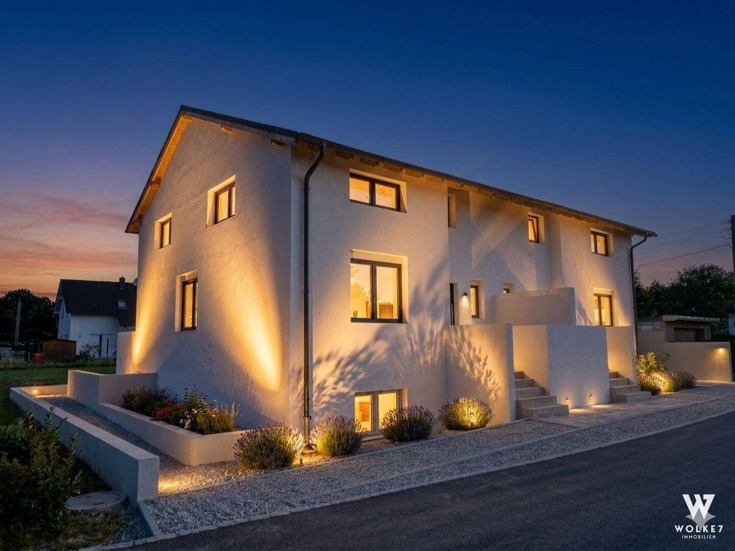 Beleuchtete moderne Hausfassade in der Abenddämmerung mit stimmungsvoller Außenbeleuchtung.