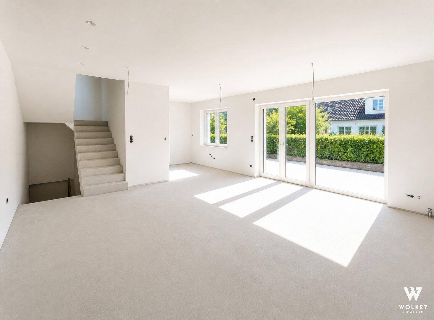 Heller, unmöblierter Wohnbereich im Rohbauzustand mit Treppe und Terrassenzugang.