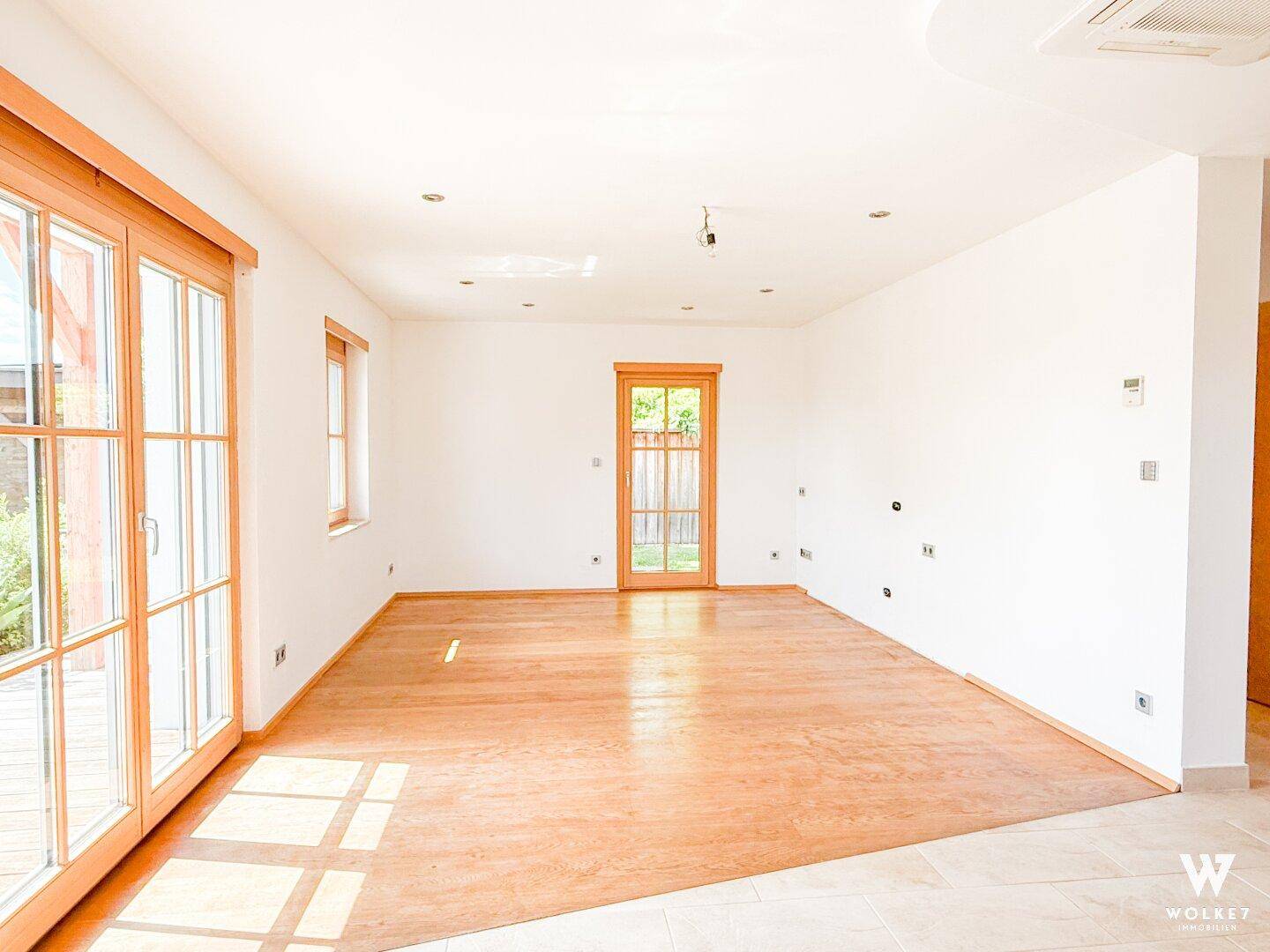 Geräumiges, unmöbliertes Wohnzimmer mit Holzboden und großen Fenstern für viel Tageslicht.