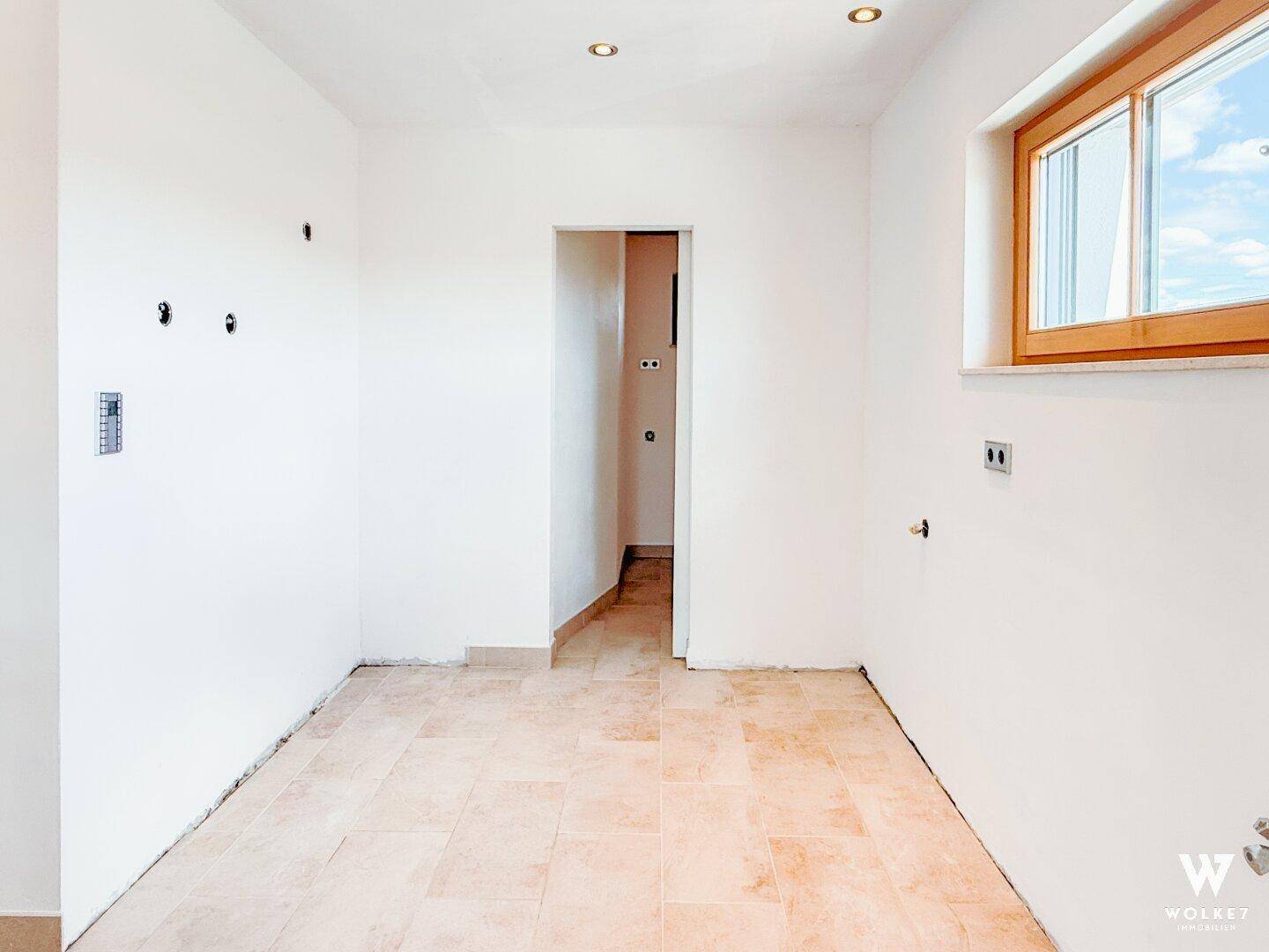 Leerer Küchenraum mit Fliesenboden und Fenster, ideal für eine individuelle Küchengestaltung.
