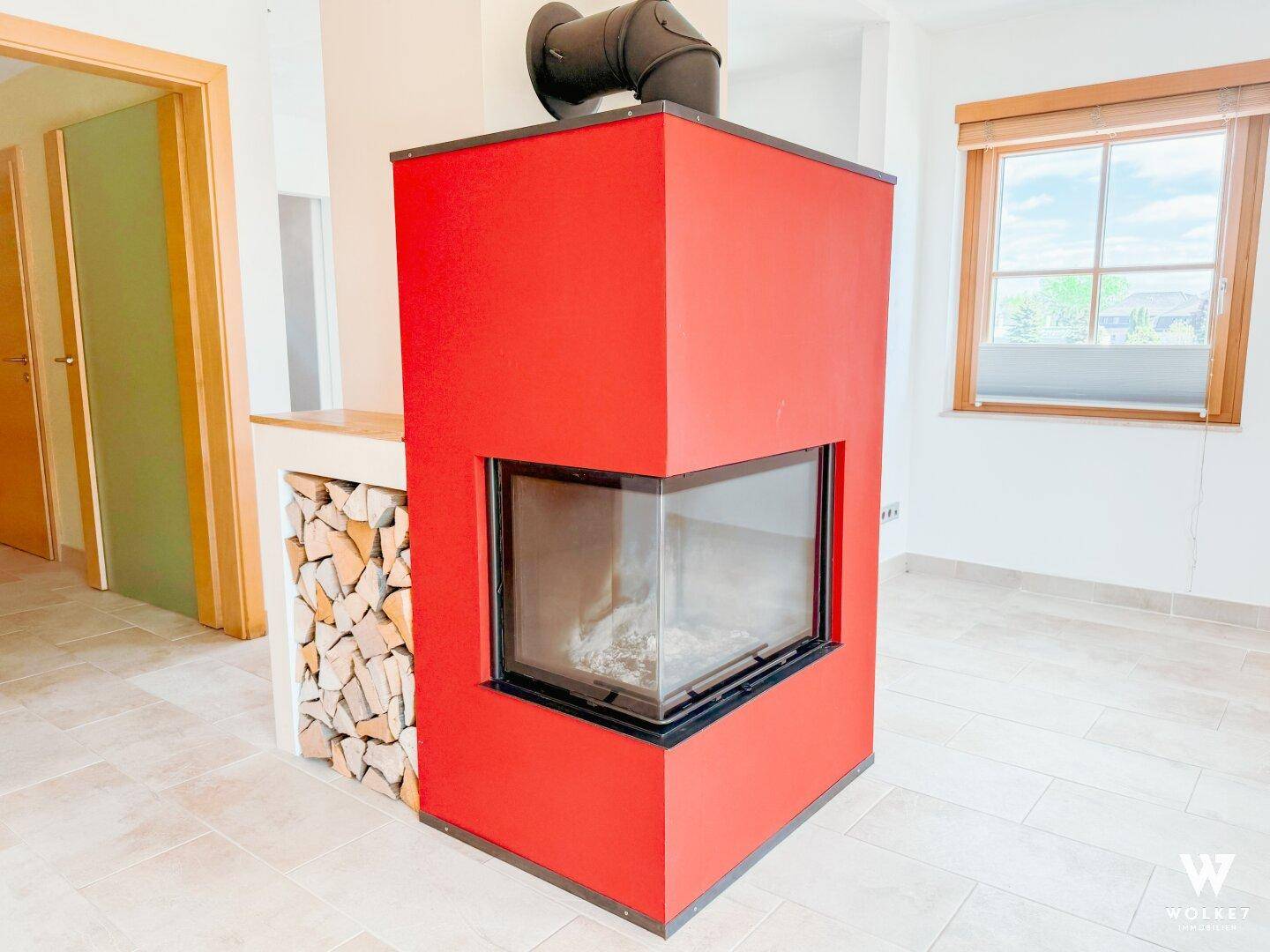 Moderner, roter Kamin als Blickfang in einem hellen Wohnbereich mit Fliesenboden.