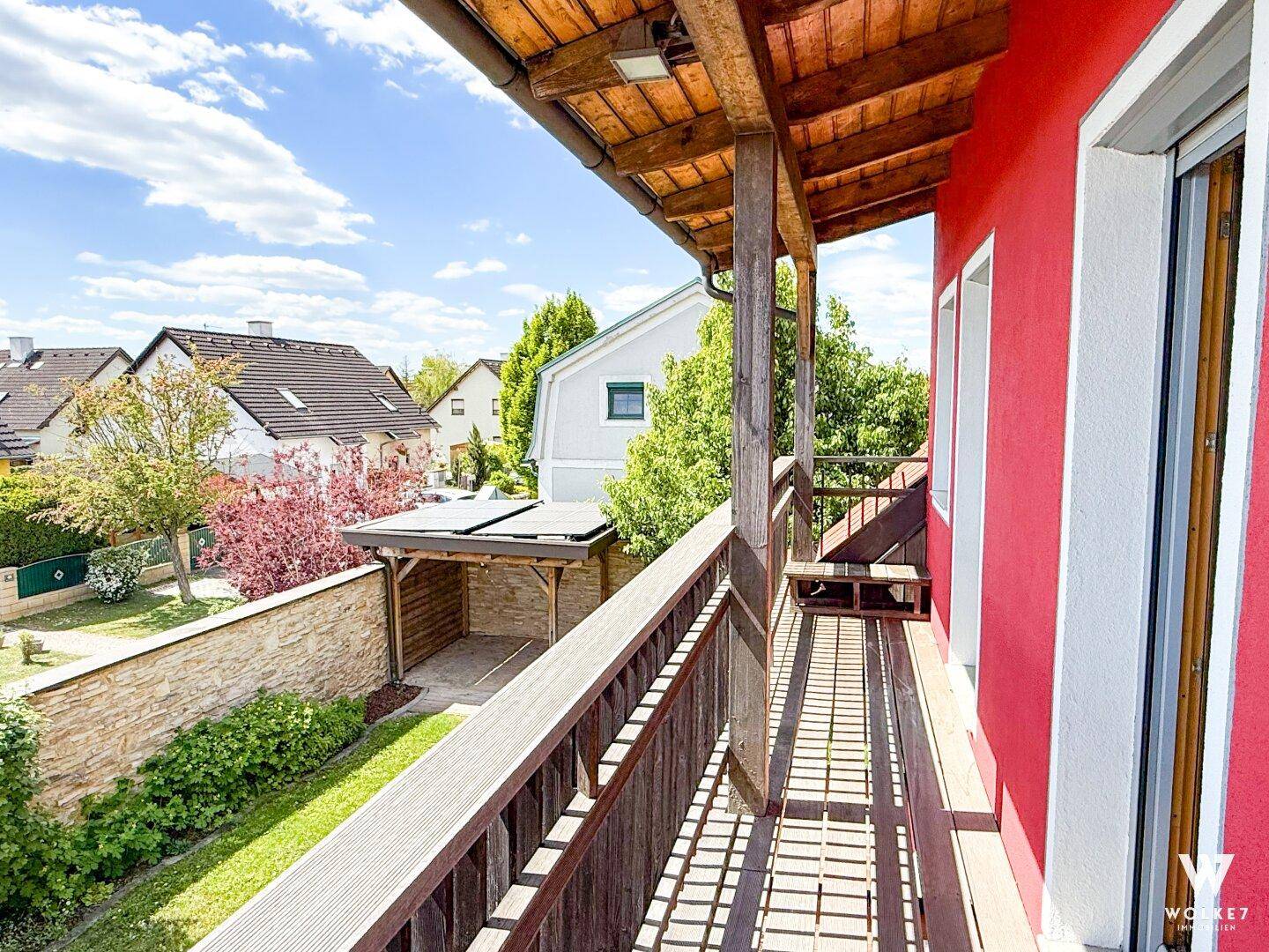 Überdachter Balkon mit Holzboden und Blick auf den Garten und die Nachbarschaft.