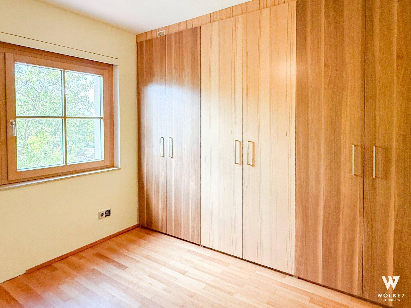 Schlafzimmer mit Einbauschränken aus Holz und Fenster, das viel Tageslicht hereinlässt.