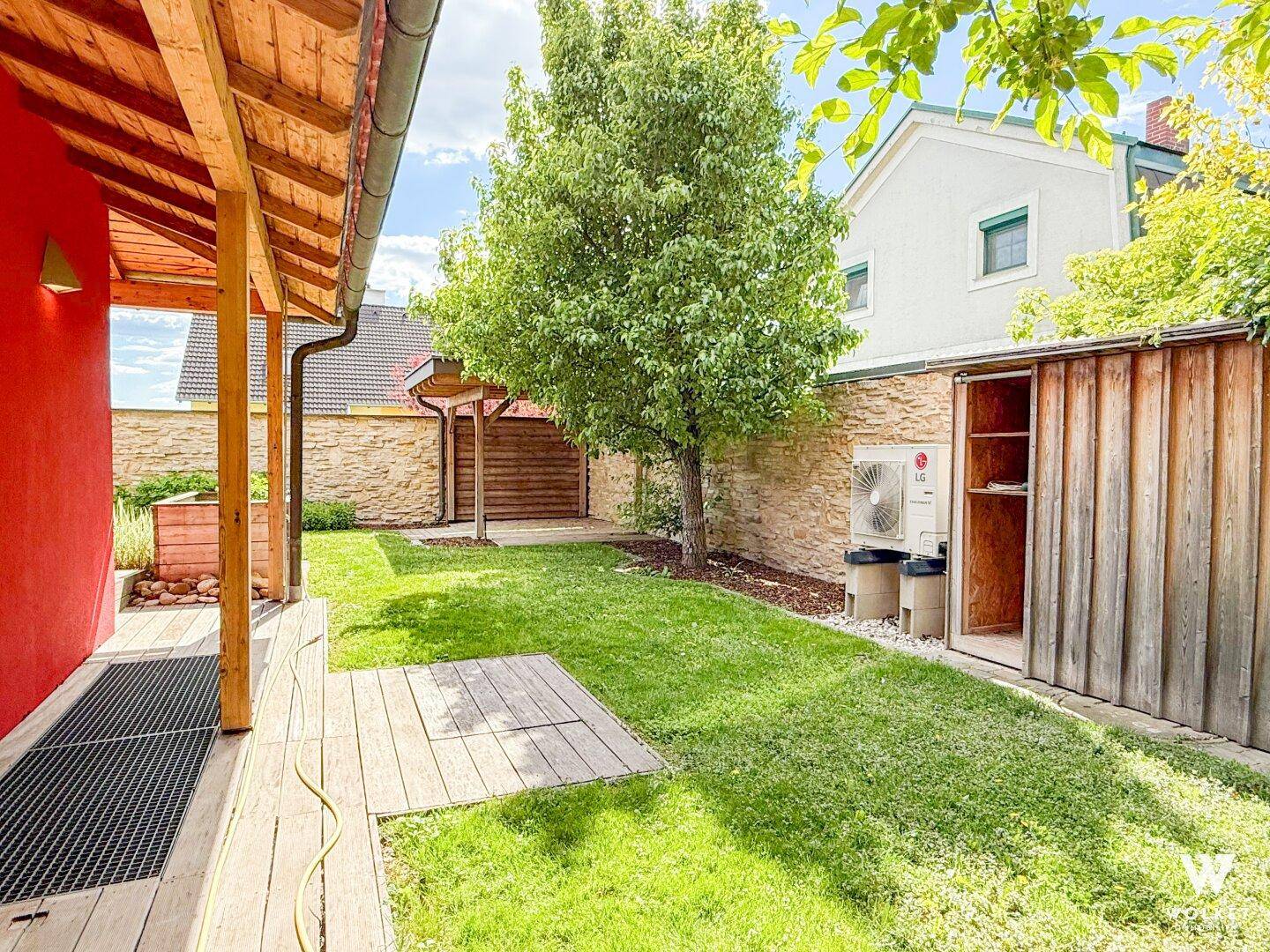 Hinterhof mit gepflegtem Rasen, einem Baum und einem Holzschuppen neben dem Haus.