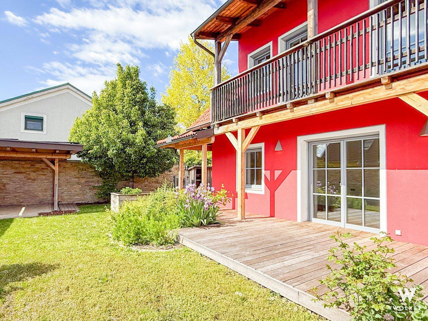 Rotes Haus mit Holzterrasse, Balkon und einem grünen Gartenbereich.