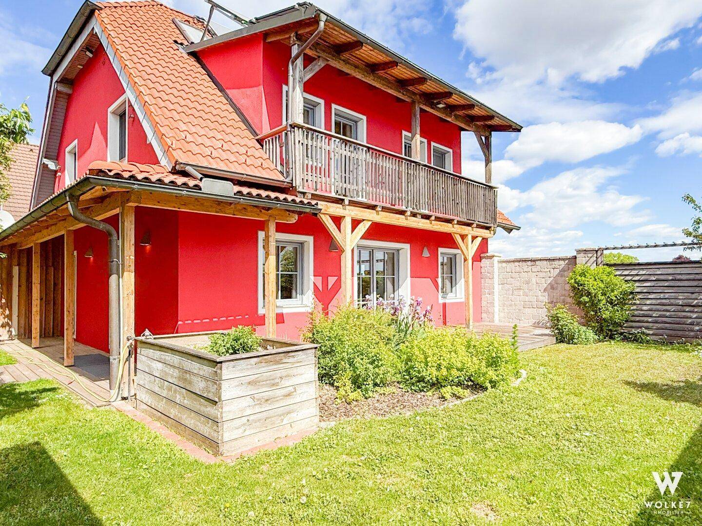 Attraktives rotes Haus mit Ziegeldach, Balkon und einem gepflegten Garten.
