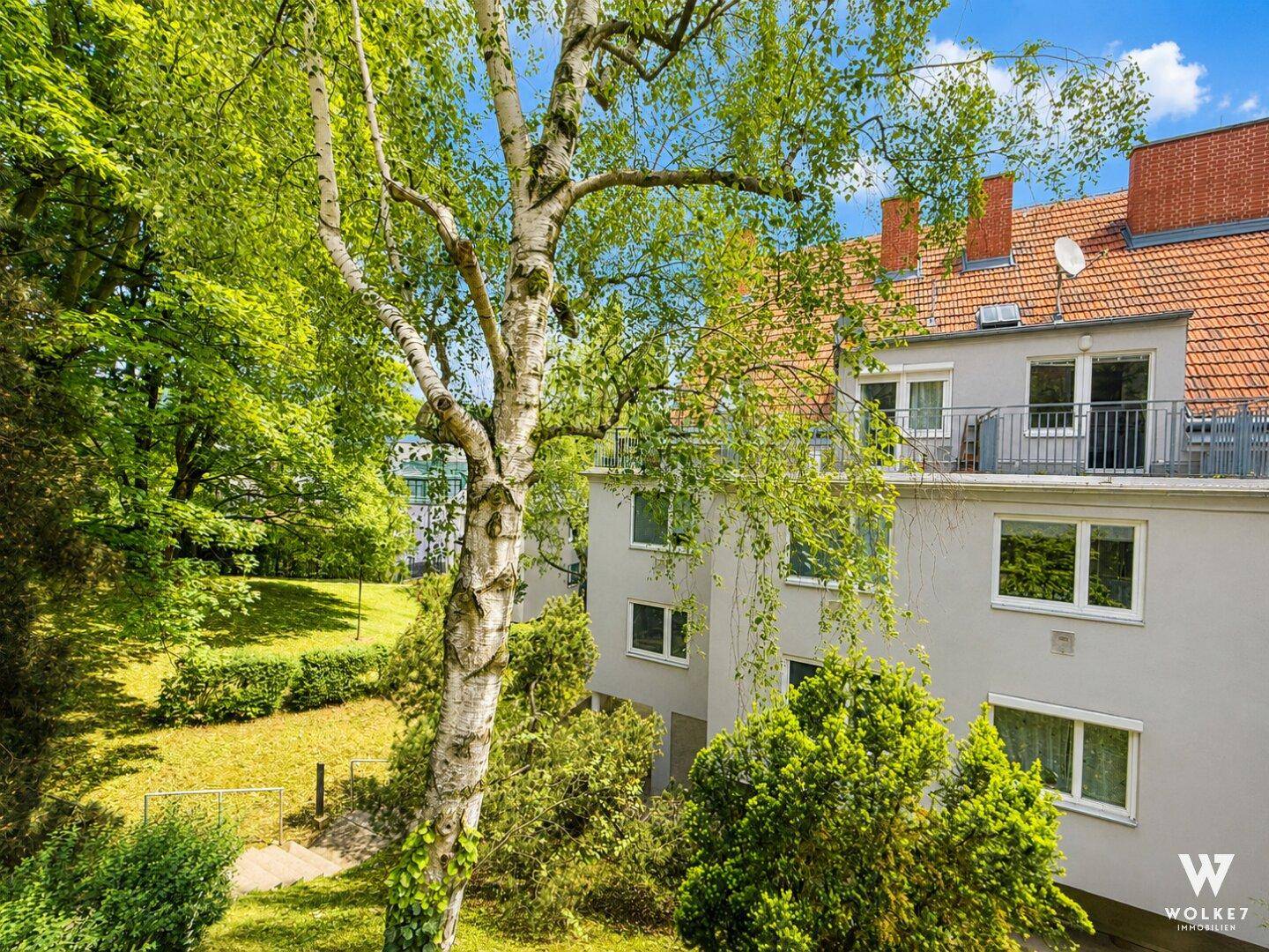Gebäudeansicht mit grüner Umgebung, Bäumen und Balkonen an der Fassade.