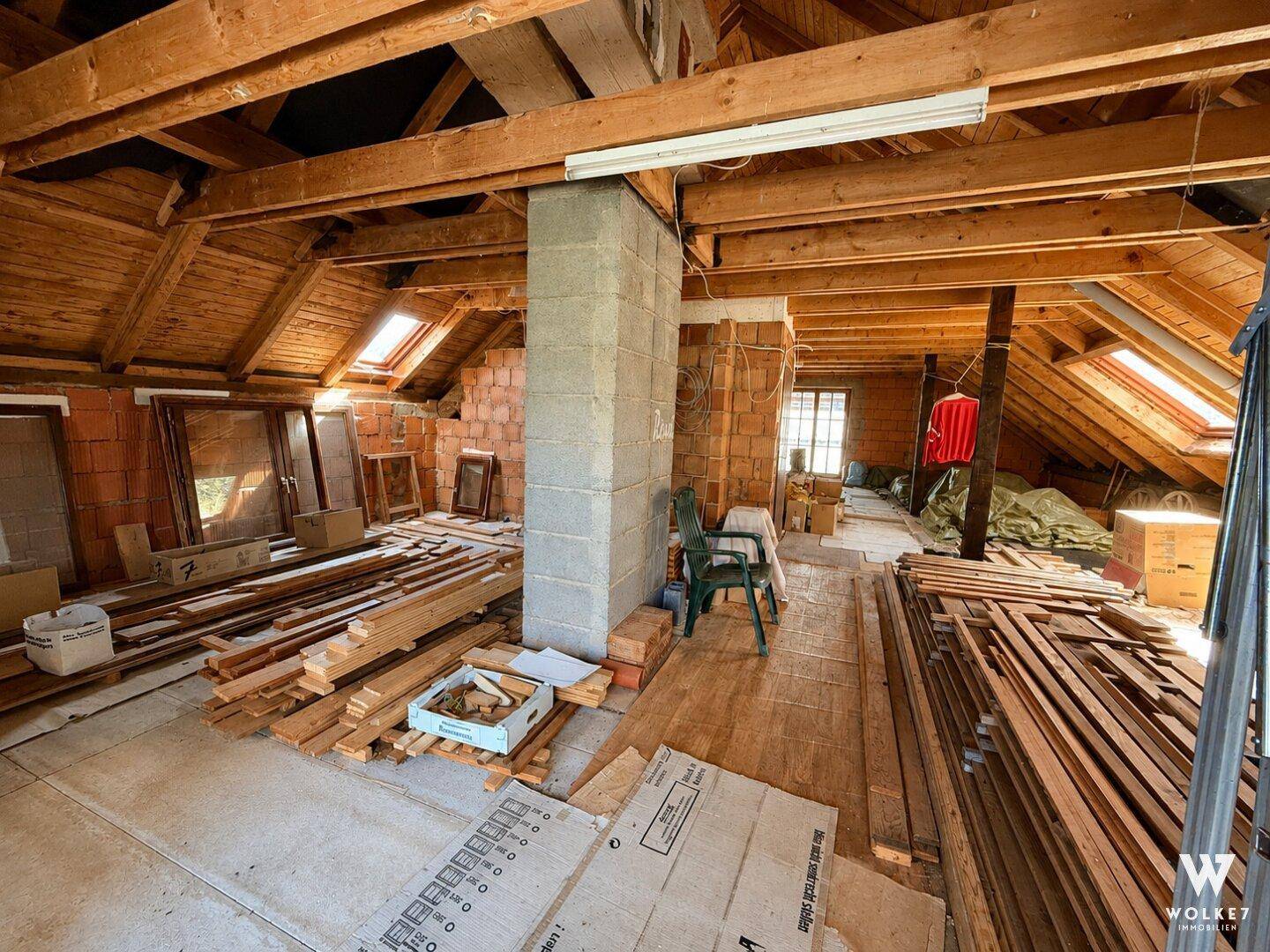 Geräumiger Dachboden im Rohbau mit Holzbalken und Baumaterialien zur Fertigstellung.