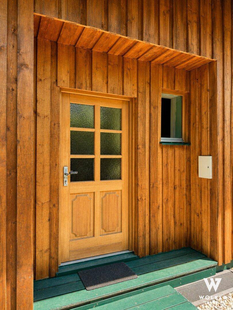 Rustikale Holzeingangstür mit kleinen Fenstern und schützendem Vordach.