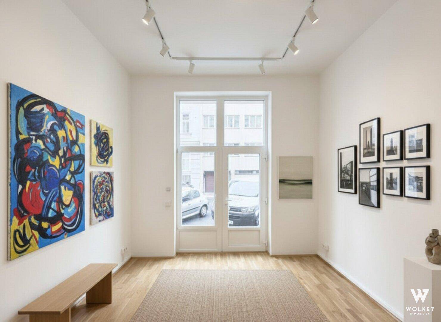 Kunstgalerie mit verschiedenen Gemälden, Holzboden und Blick durch die Fenstertüren auf die Straße.