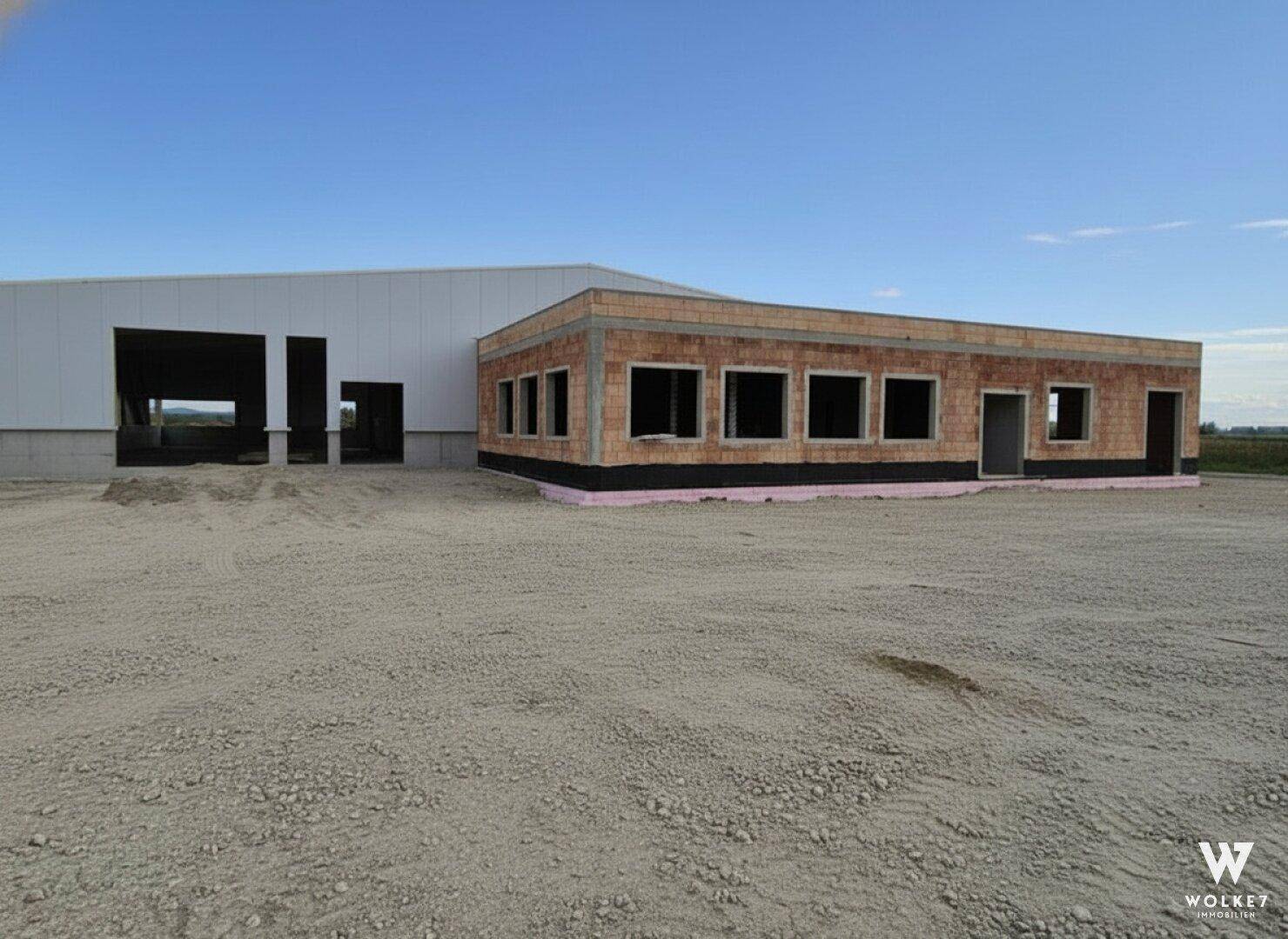 Rohbau eines Geschäftsgebäudes mit Ziegelwänden und offener Fassade auf einem Schottergrundstück im Bau.