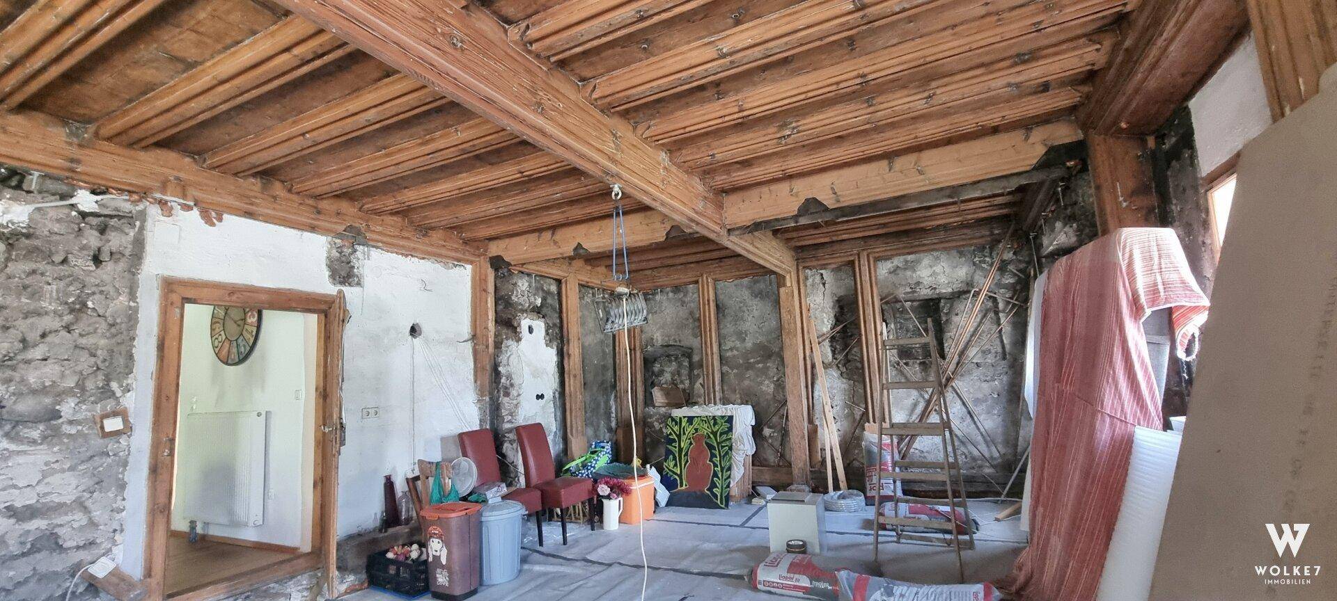 Innenraum im Rohbau mit sichtbaren Holzbalken und rustikalen Wänden, bereit zur Renovierung.