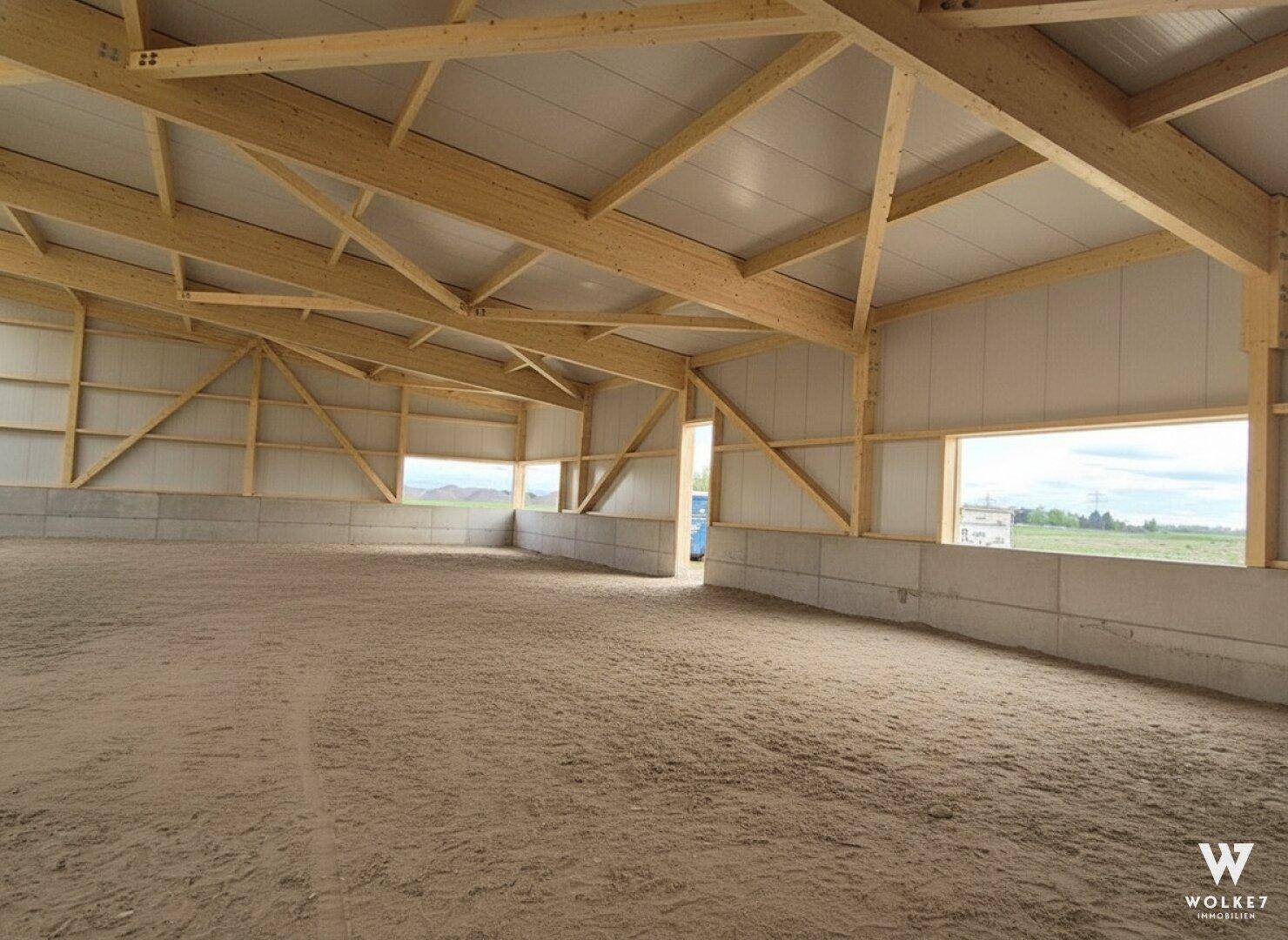 Große, leere Halle im Rohbau mit sichtbarer Holzkonstruktion und Sandboden, bereit für den Ausbau.