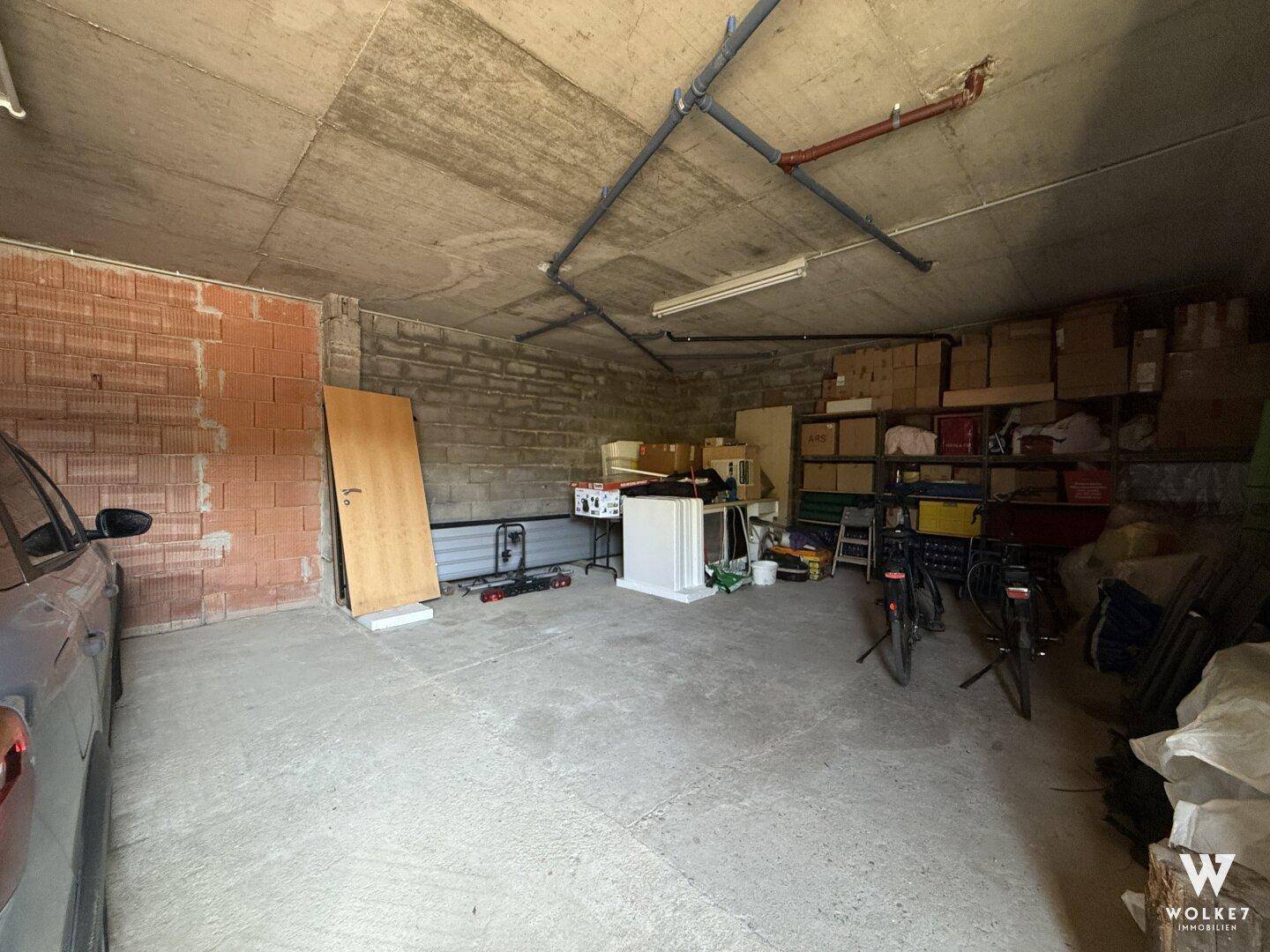 Große Garage mit Betonboden, unverputzten Wänden und viel Stauraum für Fahrzeuge und Gegenstände.