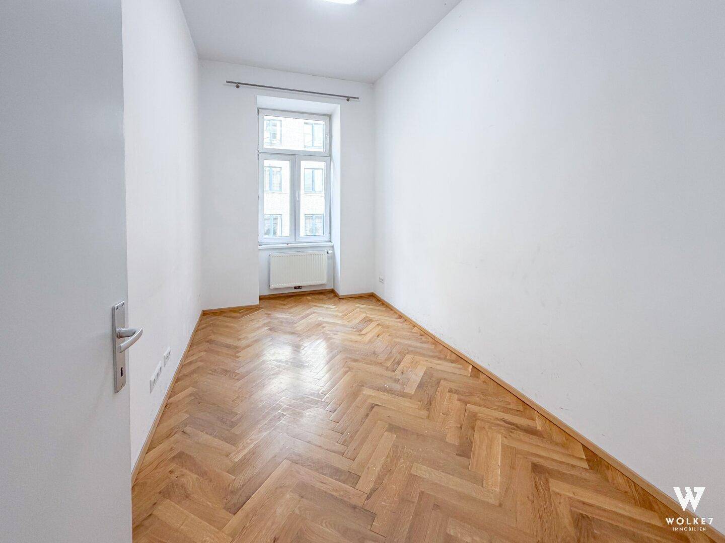 Leeres Schlafzimmer mit Fischgrätparkett und einem Fenster, bereit zur Einrichtung.