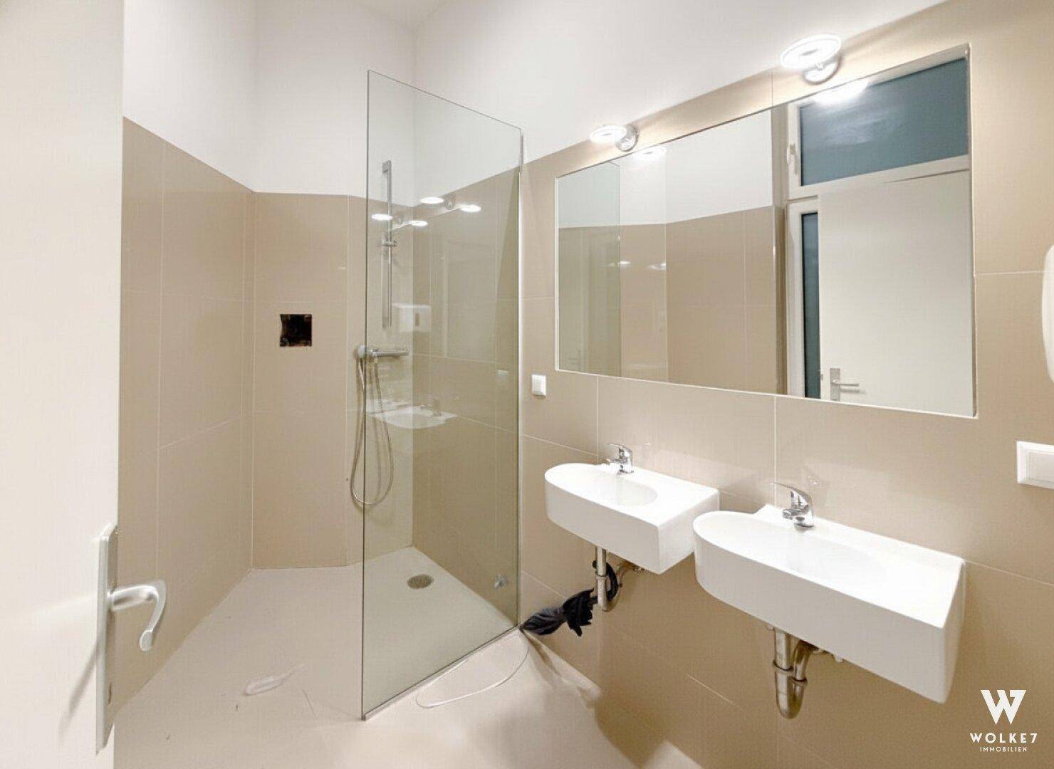 Modernes Badezimmer mit zwei Waschbecken, großer Glasdusche und hellen Fliesen.