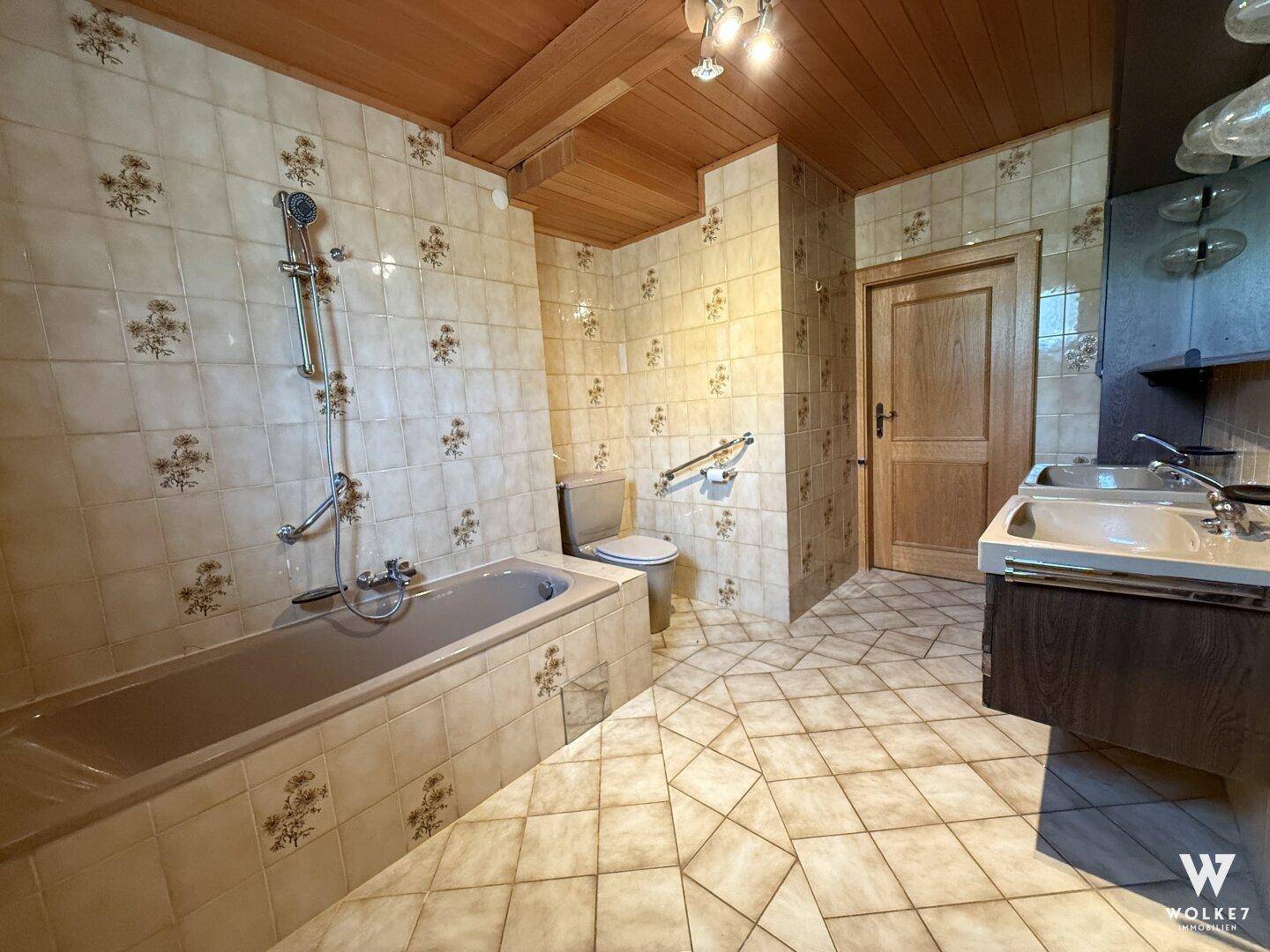 Traditionelles Badezimmer mit gemusterten Fliesen, Badewanne und Doppelwaschbecken.