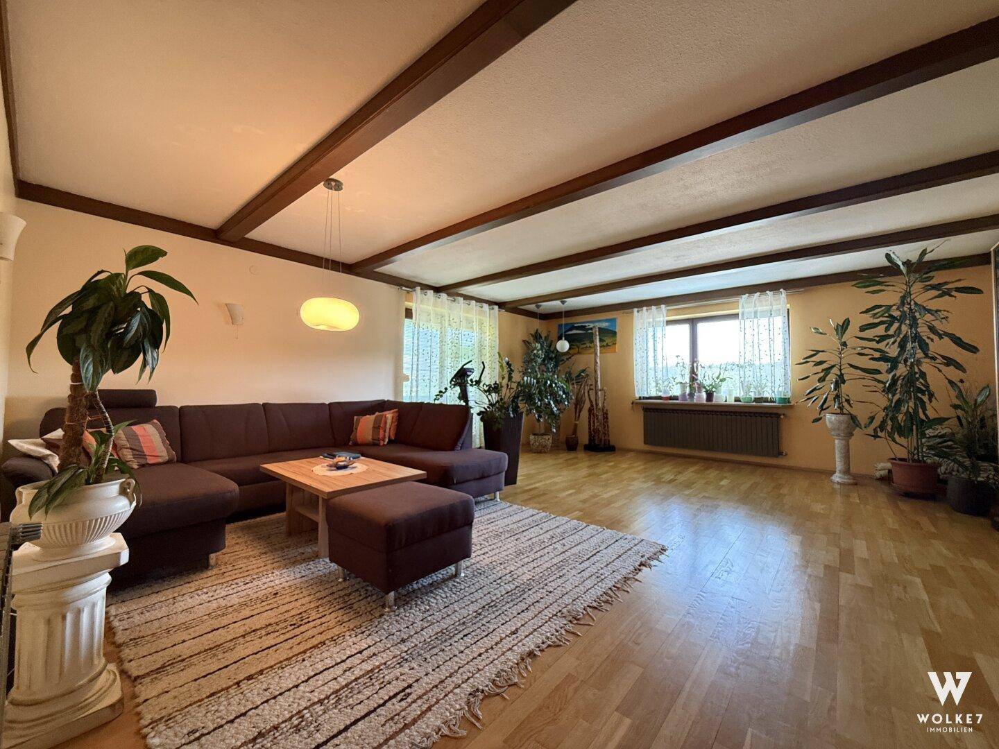 Geräumiges Wohnzimmer mit Holzbalkendecke, Parkettboden und vielen Pflanzen.