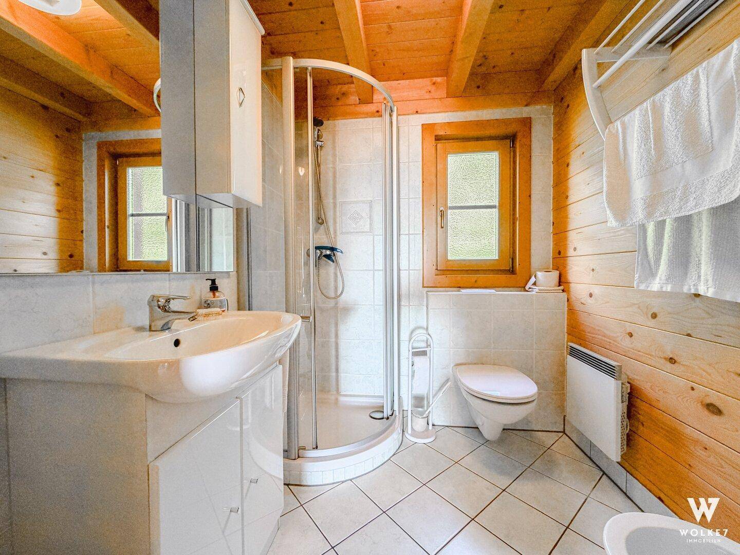 Helles Badezimmer mit Duschkabine, Waschbecken und WC, komplett gefliest.