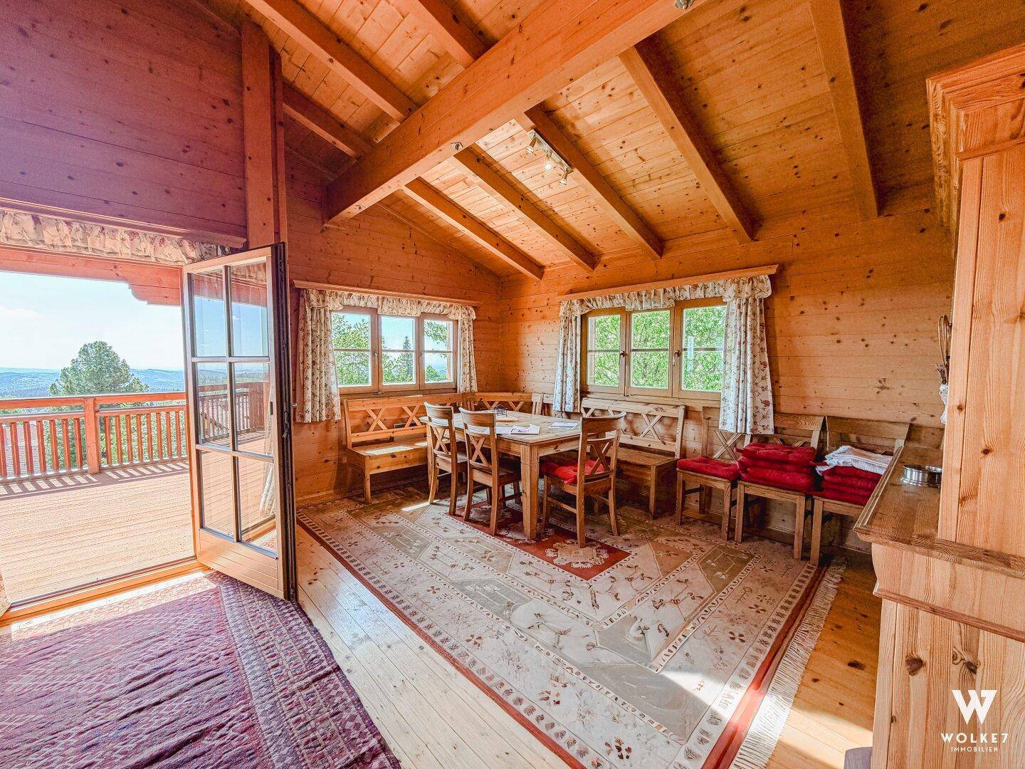 Heller Essbereich mit Holztisch und Bänken, Holzwänden und Zugang zu einem Balkon.
