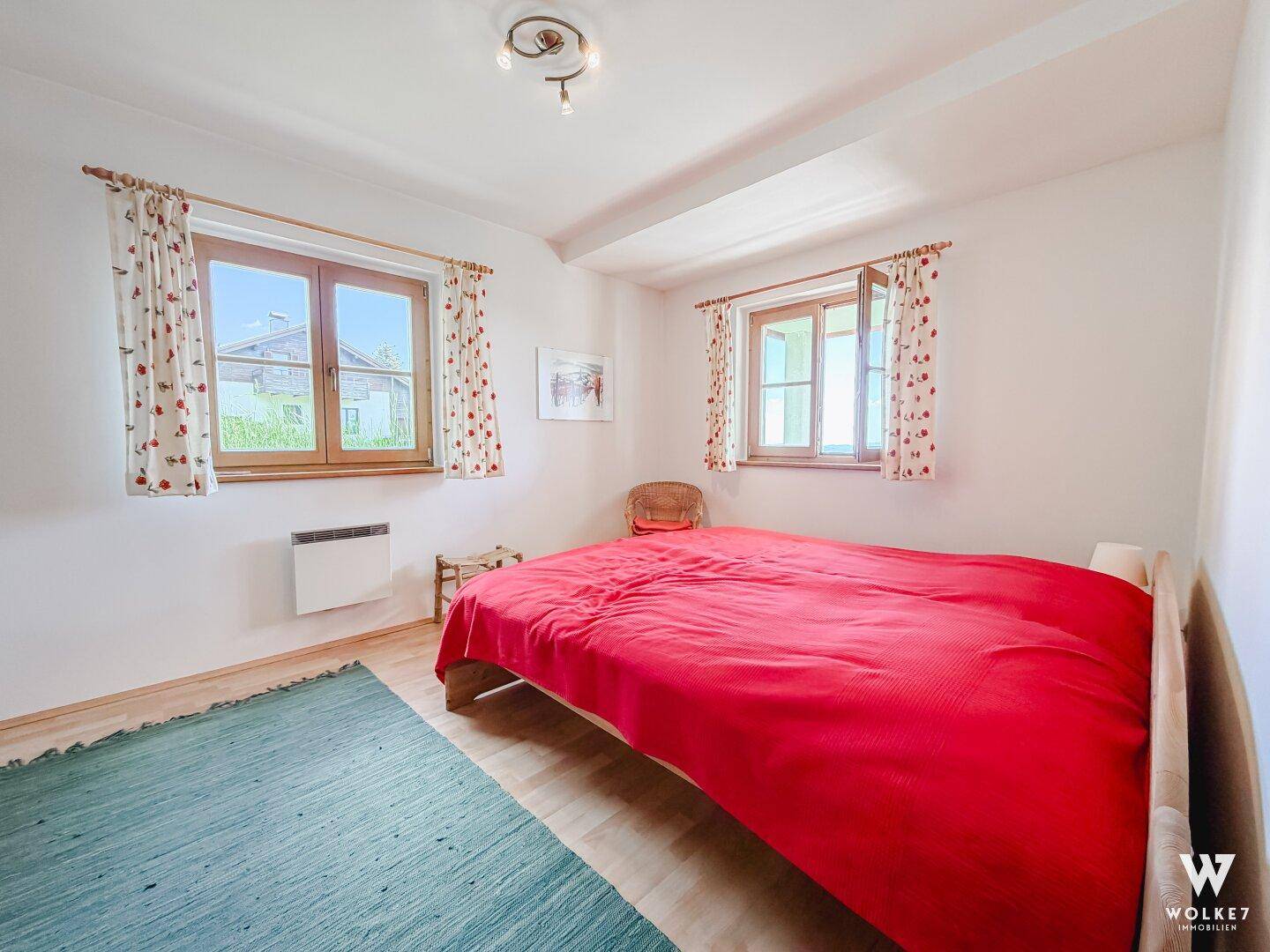Helles Schlafzimmer mit Doppelbett, weißen Wänden und zwei Fenstern.