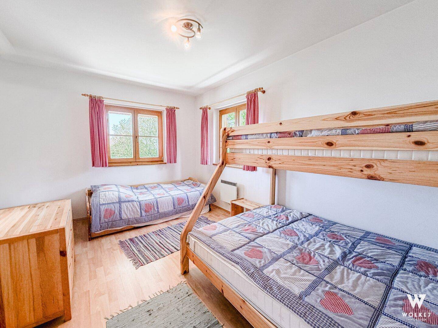 Kinderzimmer mit Etagenbett und Einzelbett, hellen Wänden und Holzfußboden.