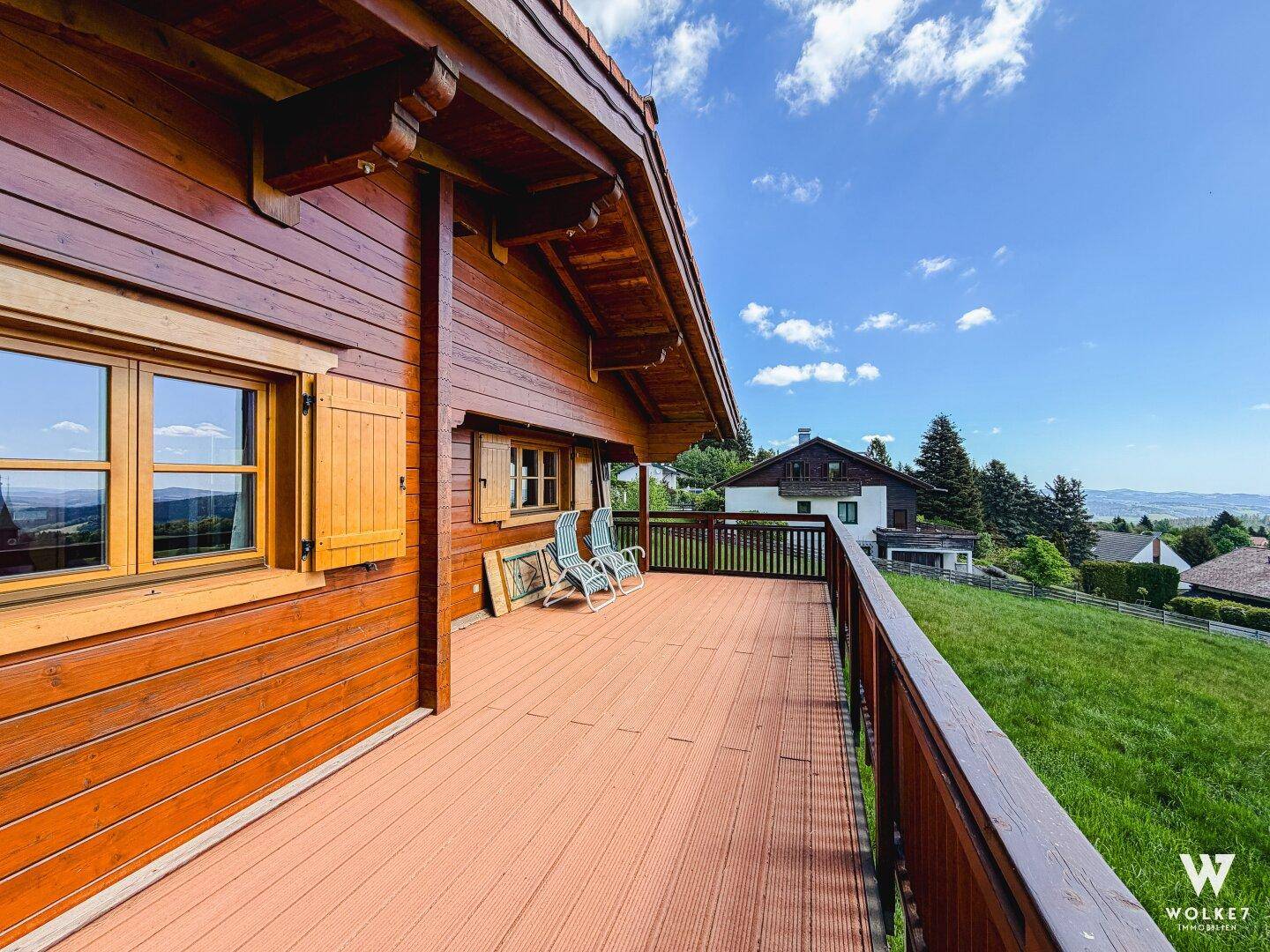 Geräumiger Holzbalkon mit Blick auf die umliegende Landschaft und Berge, ideal zum Entspannen.