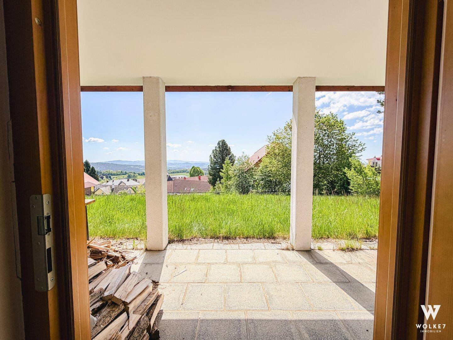Überdachte Terrasse mit Steinplatten und Blick auf die grüne Landschaft.