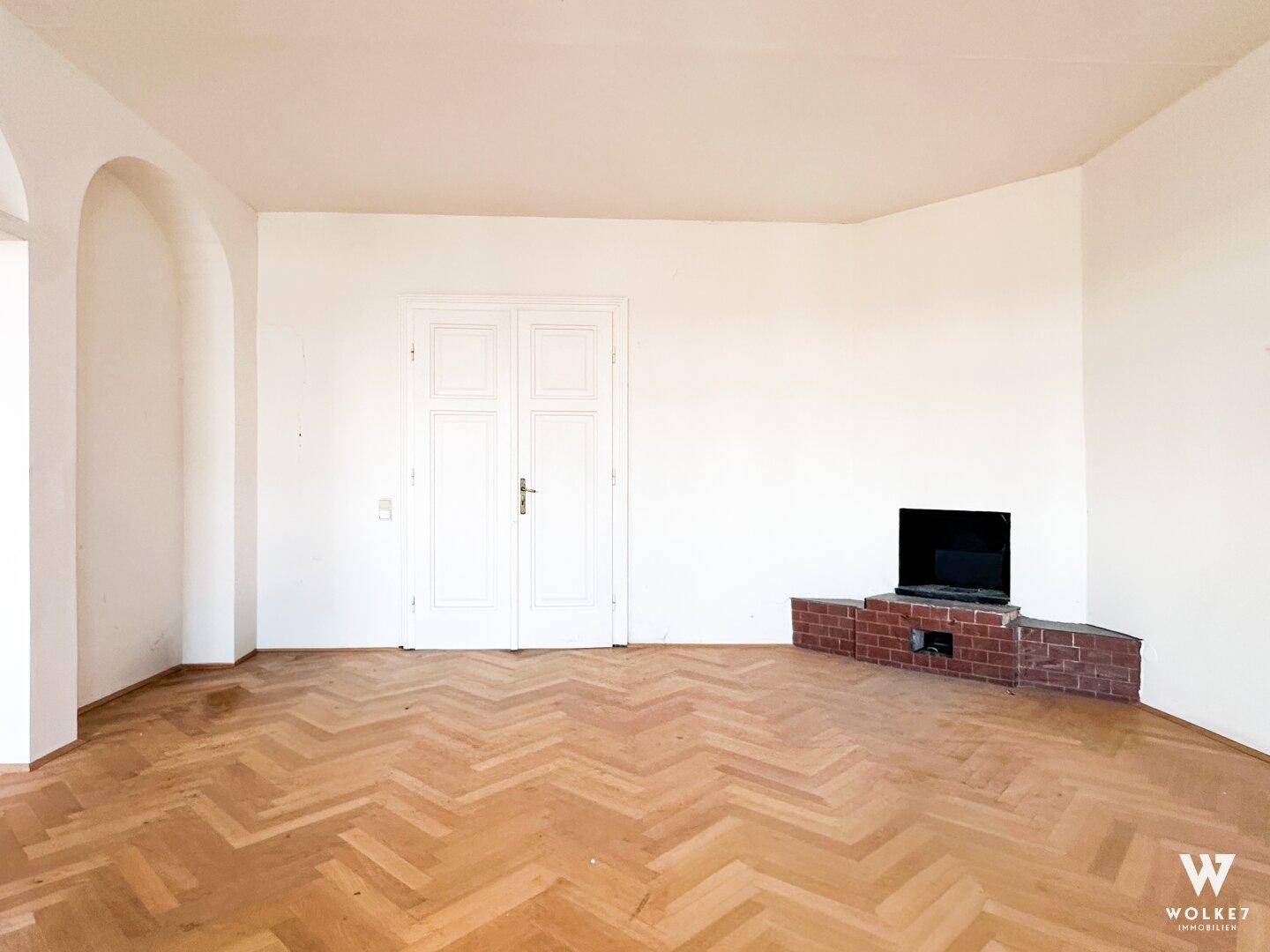 Geräumiges Zimmer mit Fischgrätparkett und einem gemauerten Kamin, ideal für gemütliche Abende.