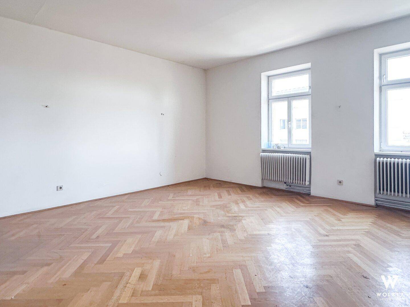 Leeres Zimmer mit Fischgrätparkett und zwei Fenstern, bereit für individuelle Gestaltung und Nutzung.