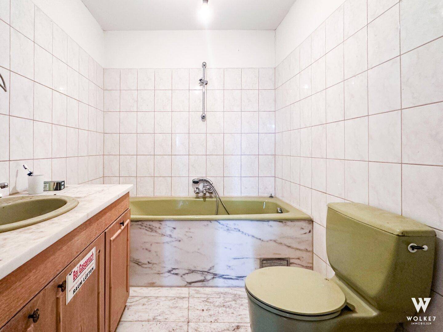 Badezimmer mit grüner Badewanne und Toilette, umgeben von weißen Fliesen, im Stil der 80er Jahre.