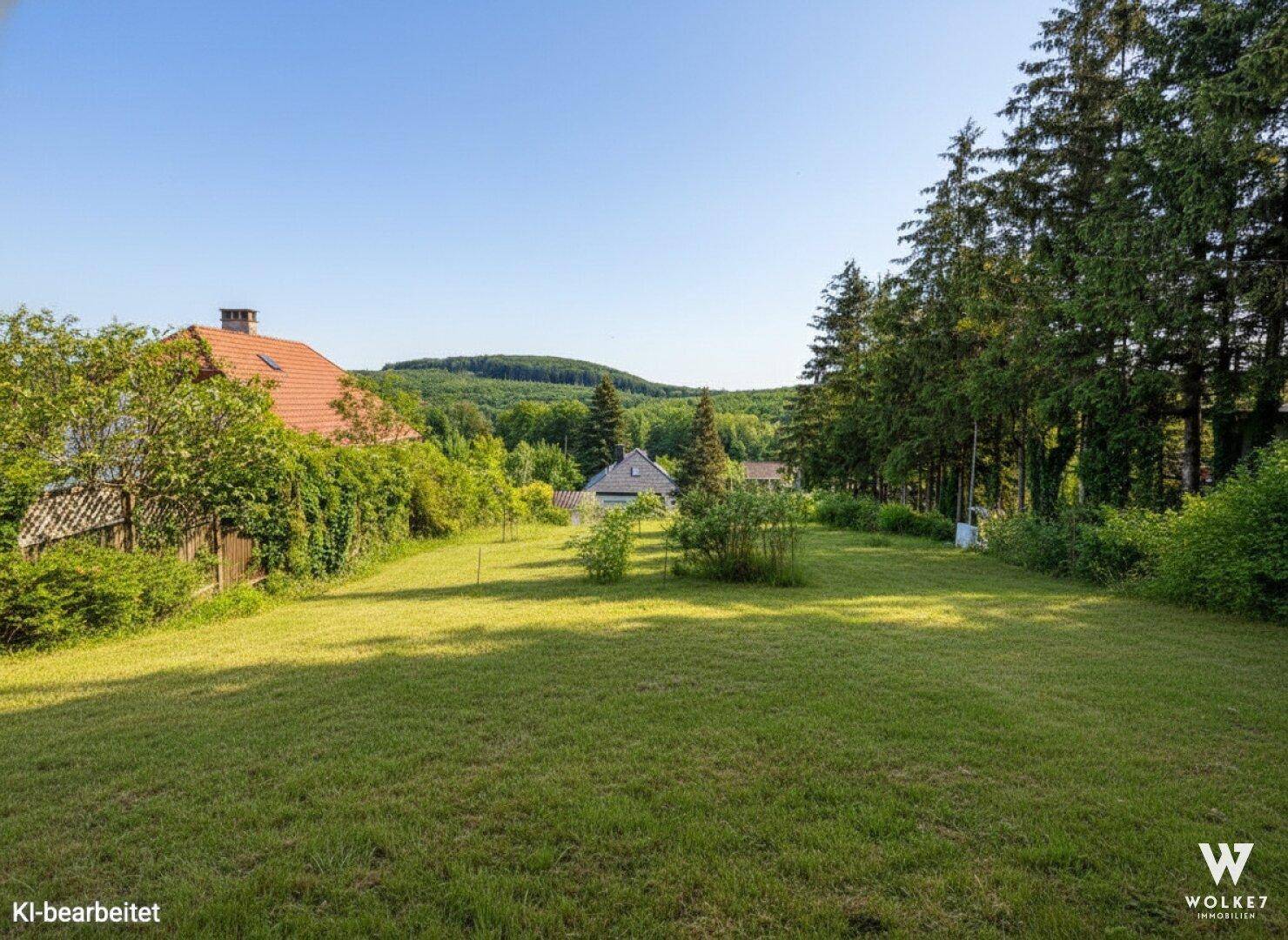 Weitläufige Rasenfläche mit Blick auf bewaldete Hügel und weitere Häuser in der Ferne.
