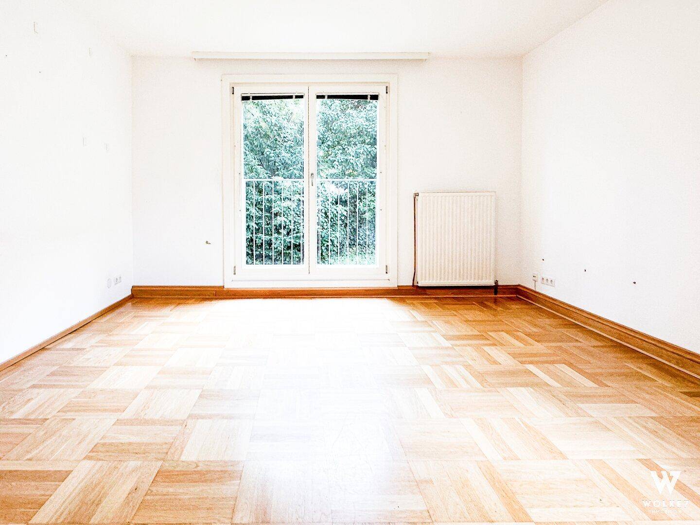 Leerer Raum mit Fischgrätparkett und einer Tür, die zu einem französischen Balkon führt.