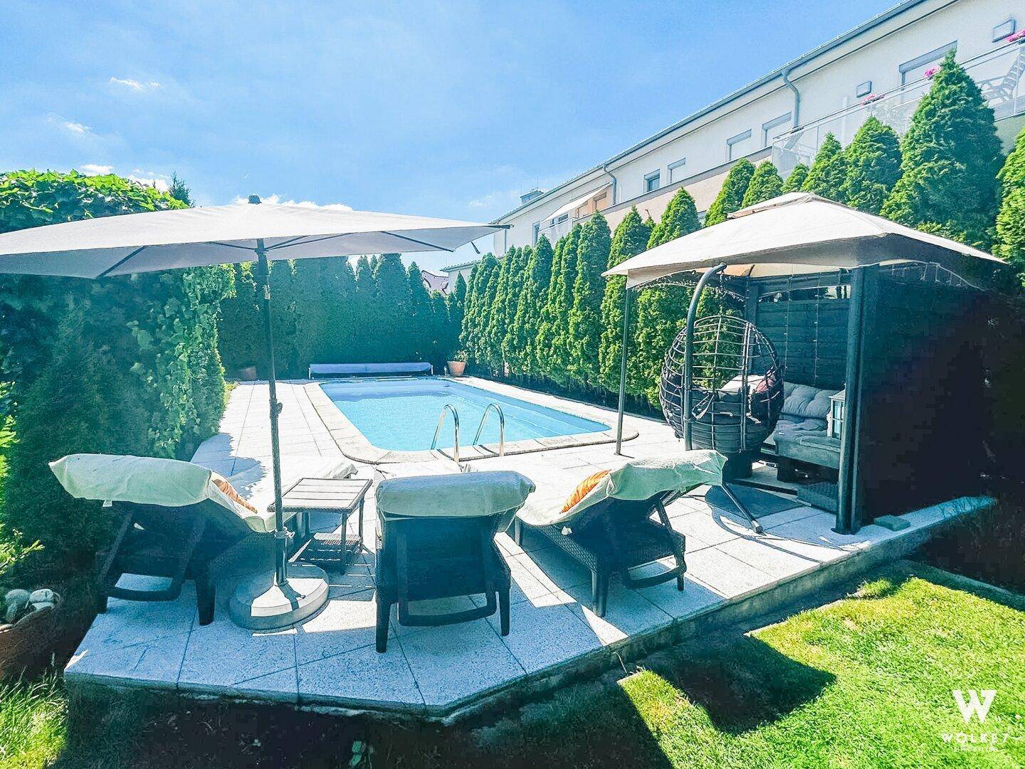 Entspannender Poolbereich mit Sonnenliegen, Sonnenschirm und einer gemütlichen Lounge-Ecke im Garten.