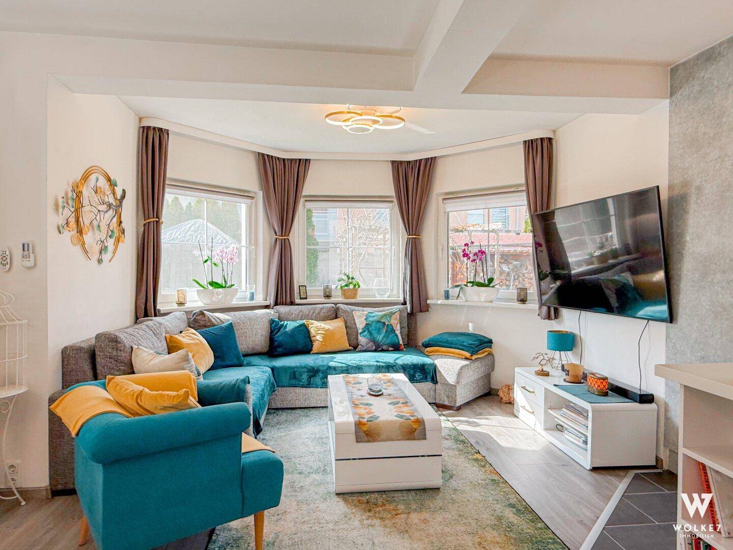 Gemütliches Wohnzimmer mit Ecksofa, farbenfrohen Kissen und einem modernen Deckenventilator.