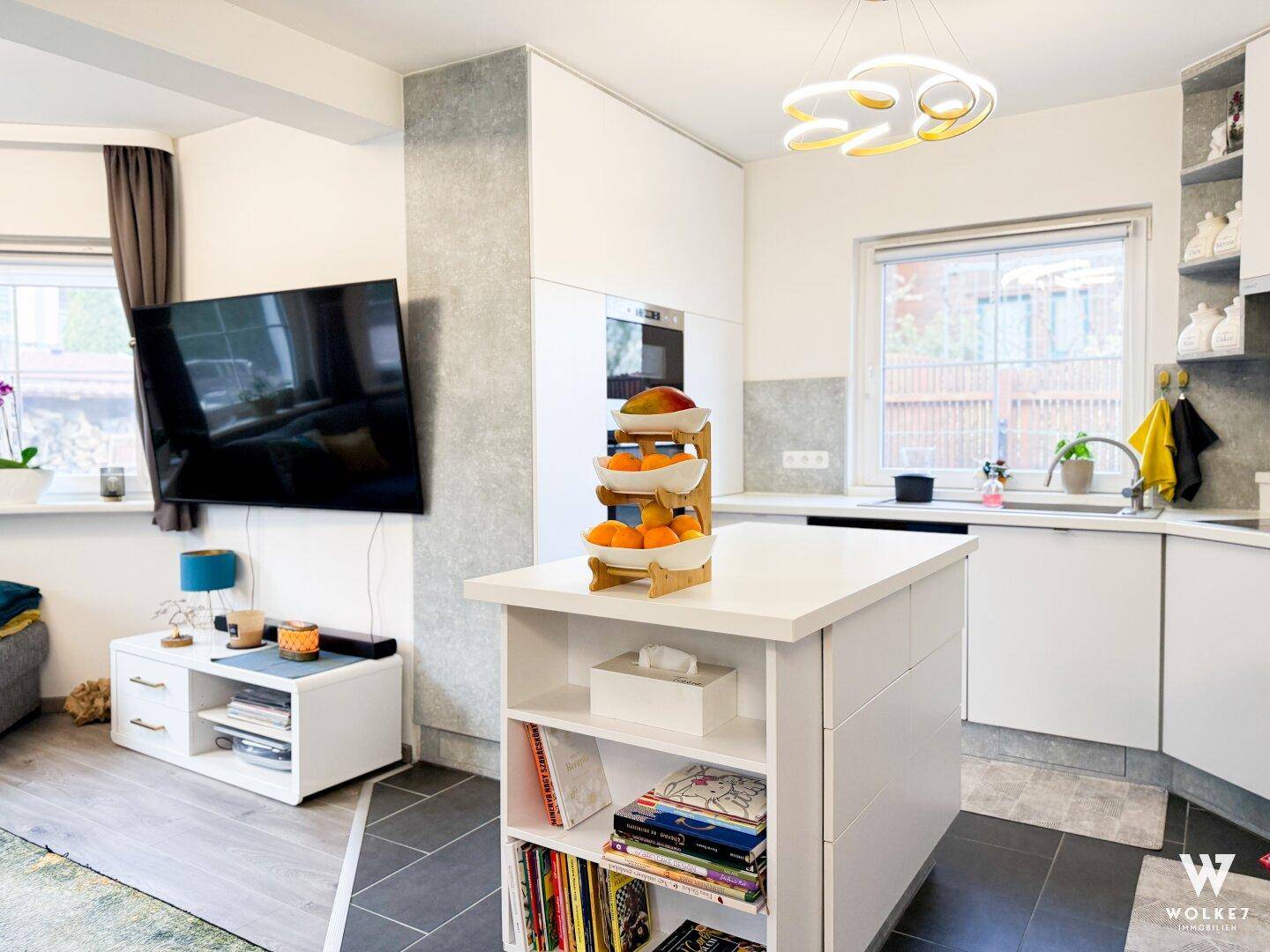 Moderne offene Küche mit weißer Kücheninsel und angrenzendem Wohnbereich mit Fernseher.