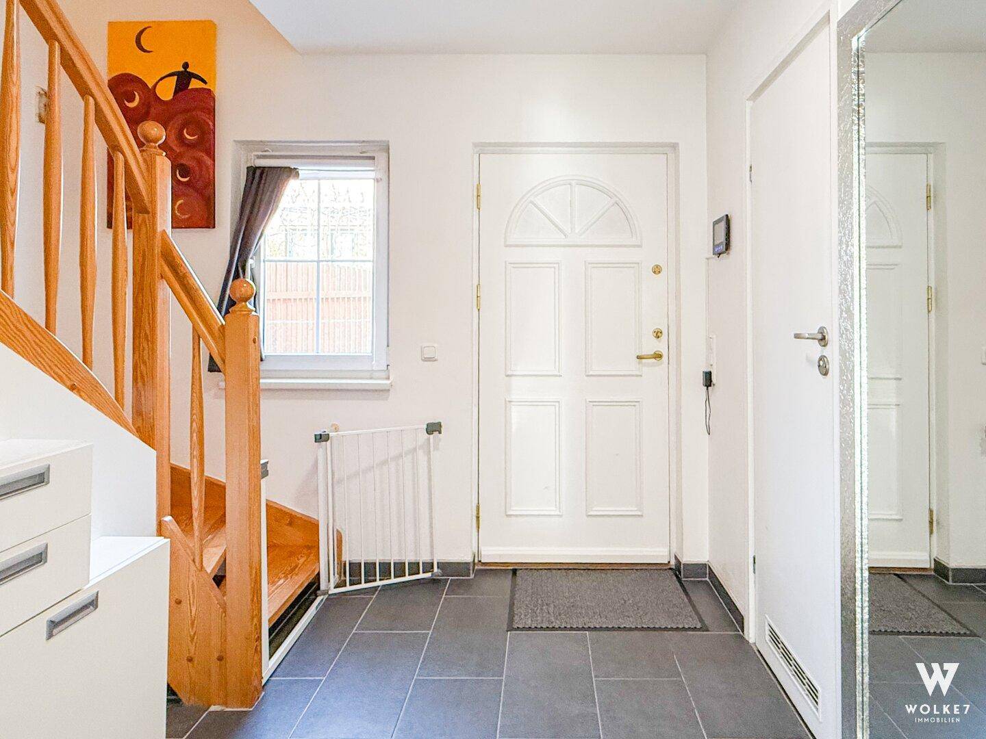 Eingangsbereich mit Fliesenboden, Holztreppe und weißer Eingangstür.