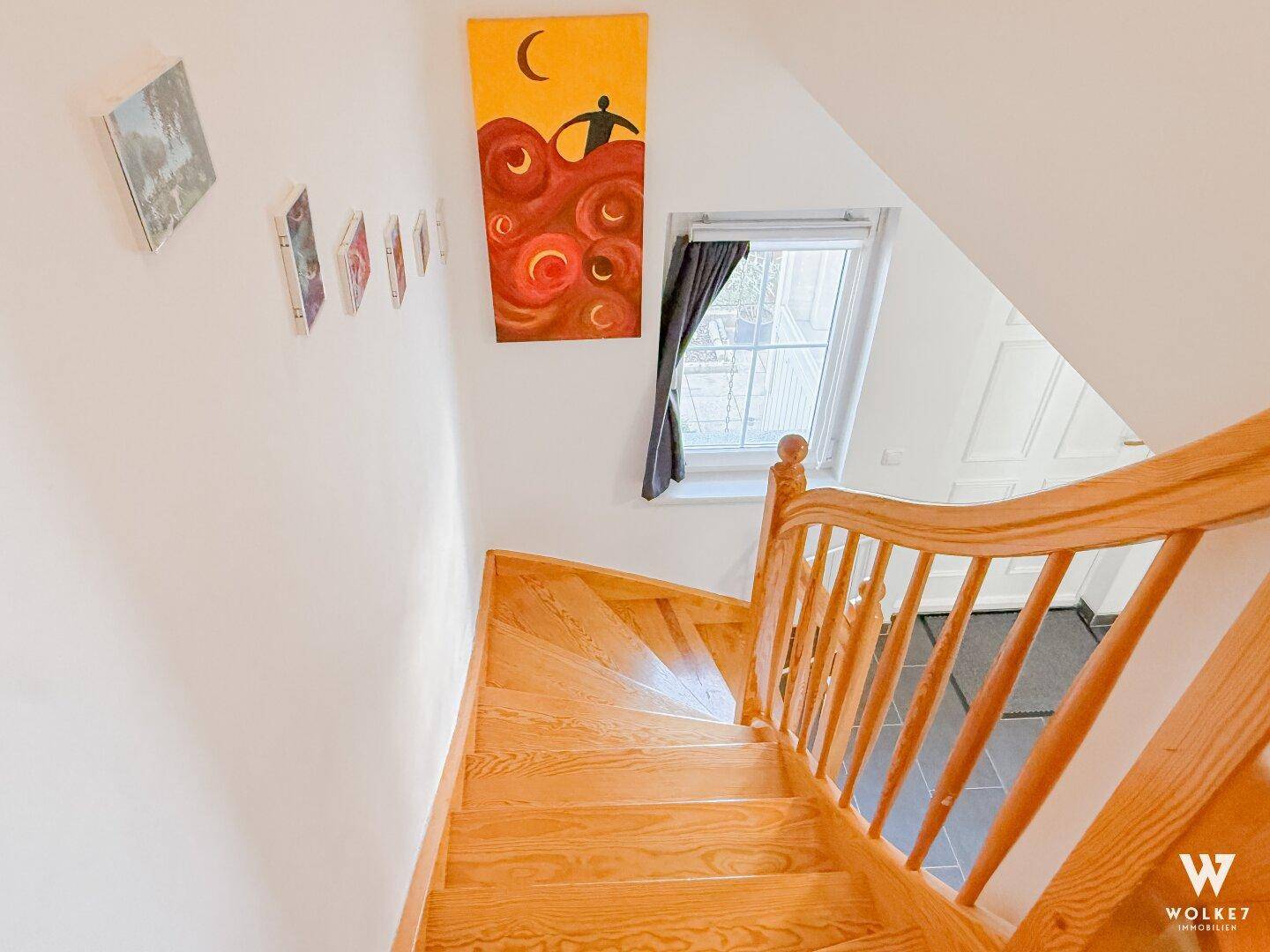 Holztreppe führt nach oben, mit einem Fenster und Kunstwerken an der Wand.