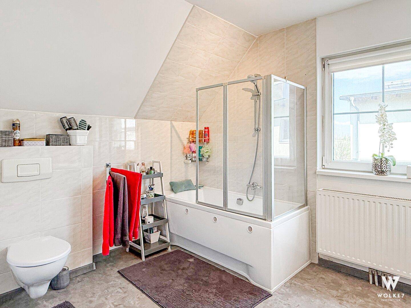 Badezimmer mit Badewanne, Duschkabine, WC und Fenster für Tageslicht.