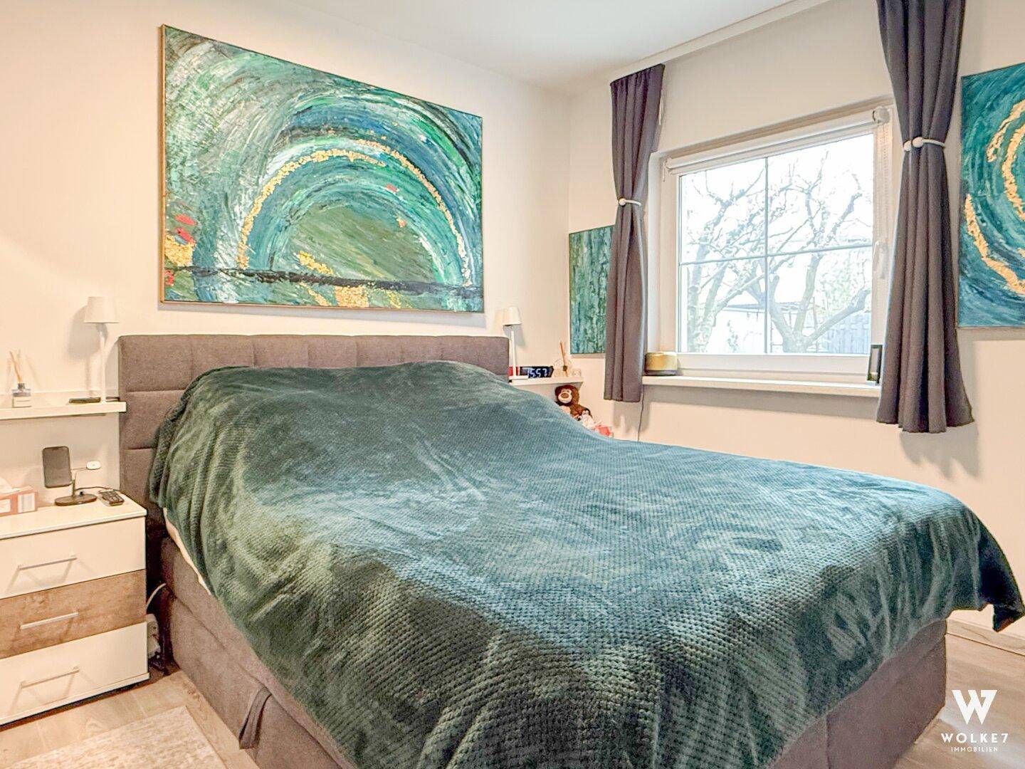 Gemütliches Schlafzimmer mit großem Bett, farbenfrohem Kunstwerk und Fensterblick.